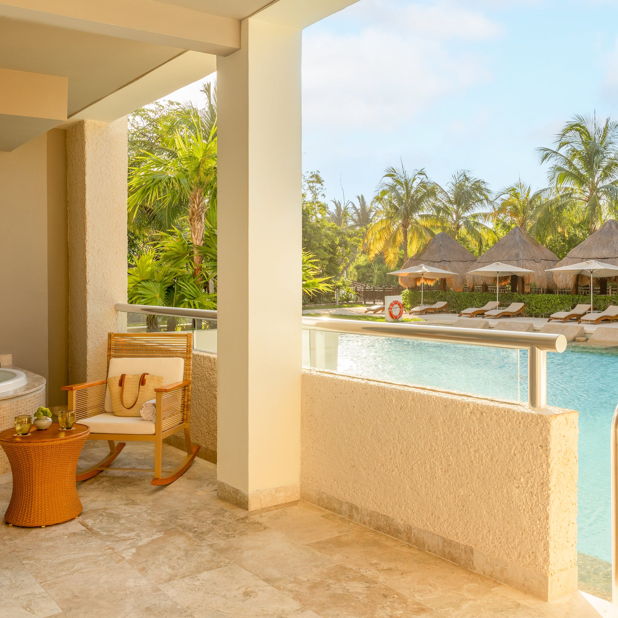 Hotel suite balcony with hot tub overlooking tropical resort pool and cabanas.