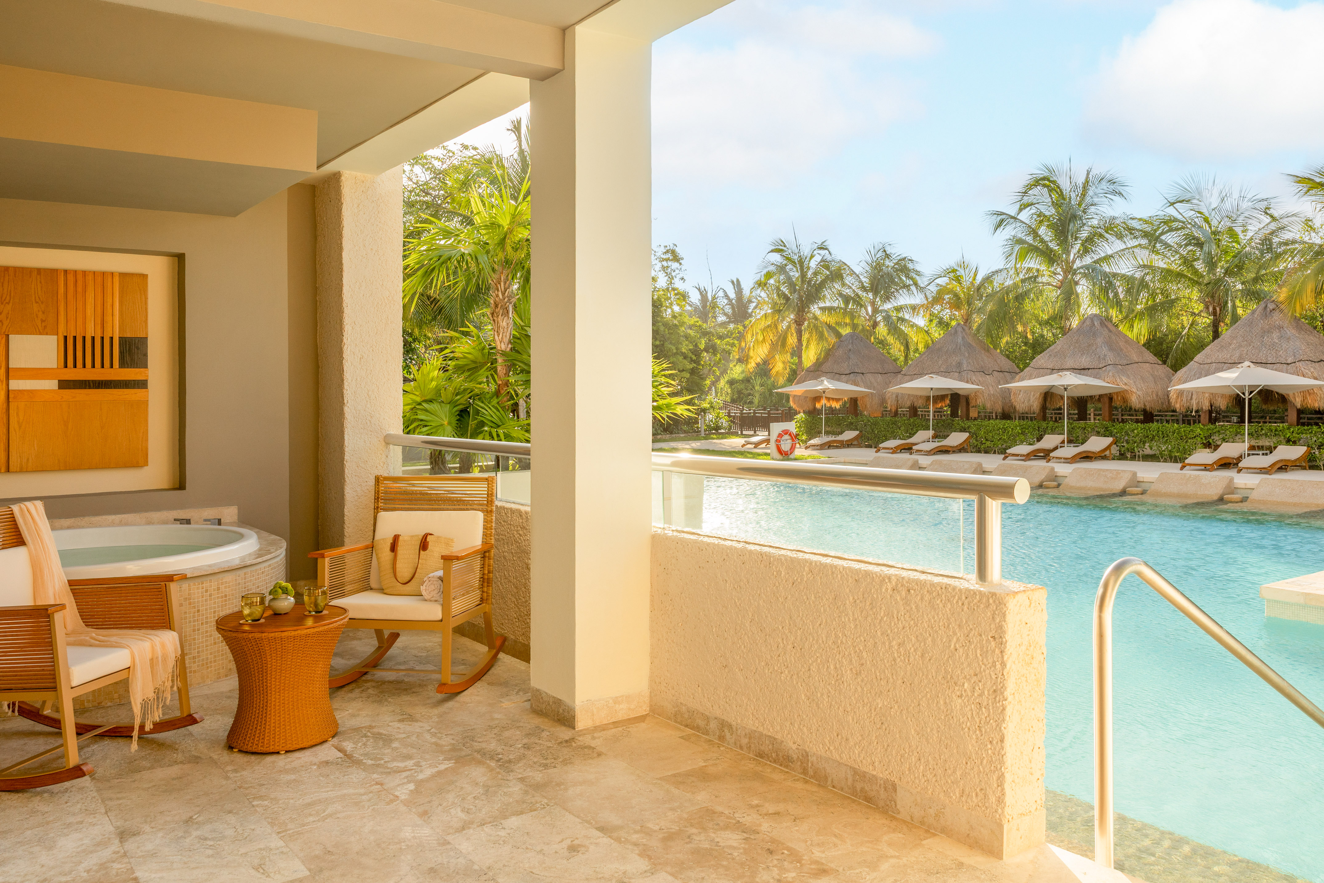 Hotel suite balcony with hot tub overlooking tropical resort pool and cabanas.