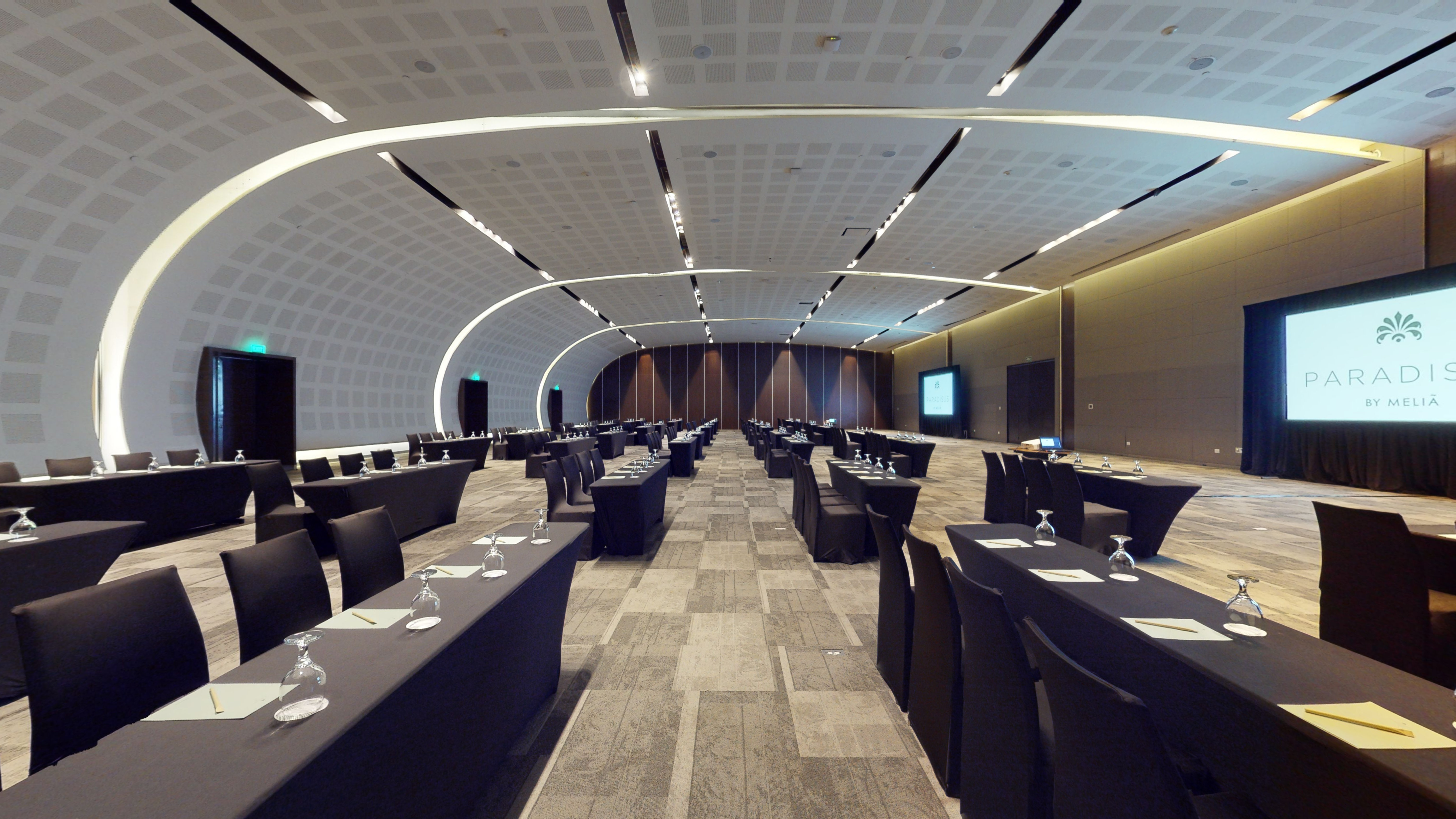Modern Paradise by Meliã meeting room setup with rows of tables & screens.