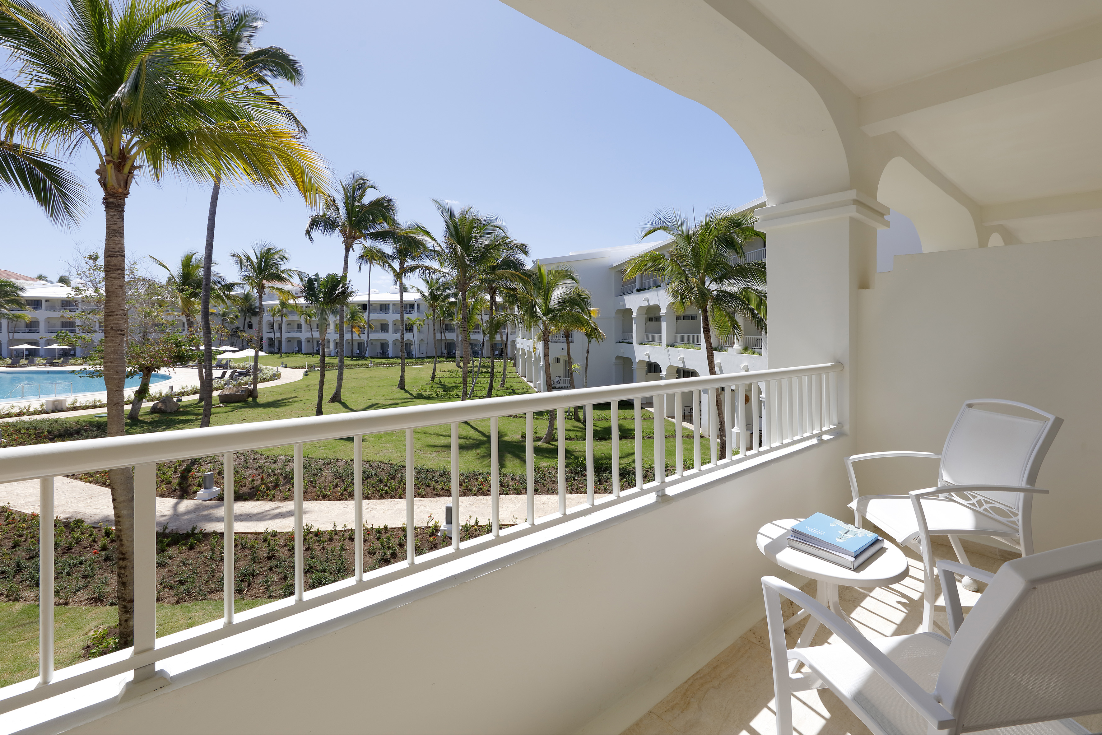 Balcony view of tropical hotel resort with palm trees, pool, and white buildings.