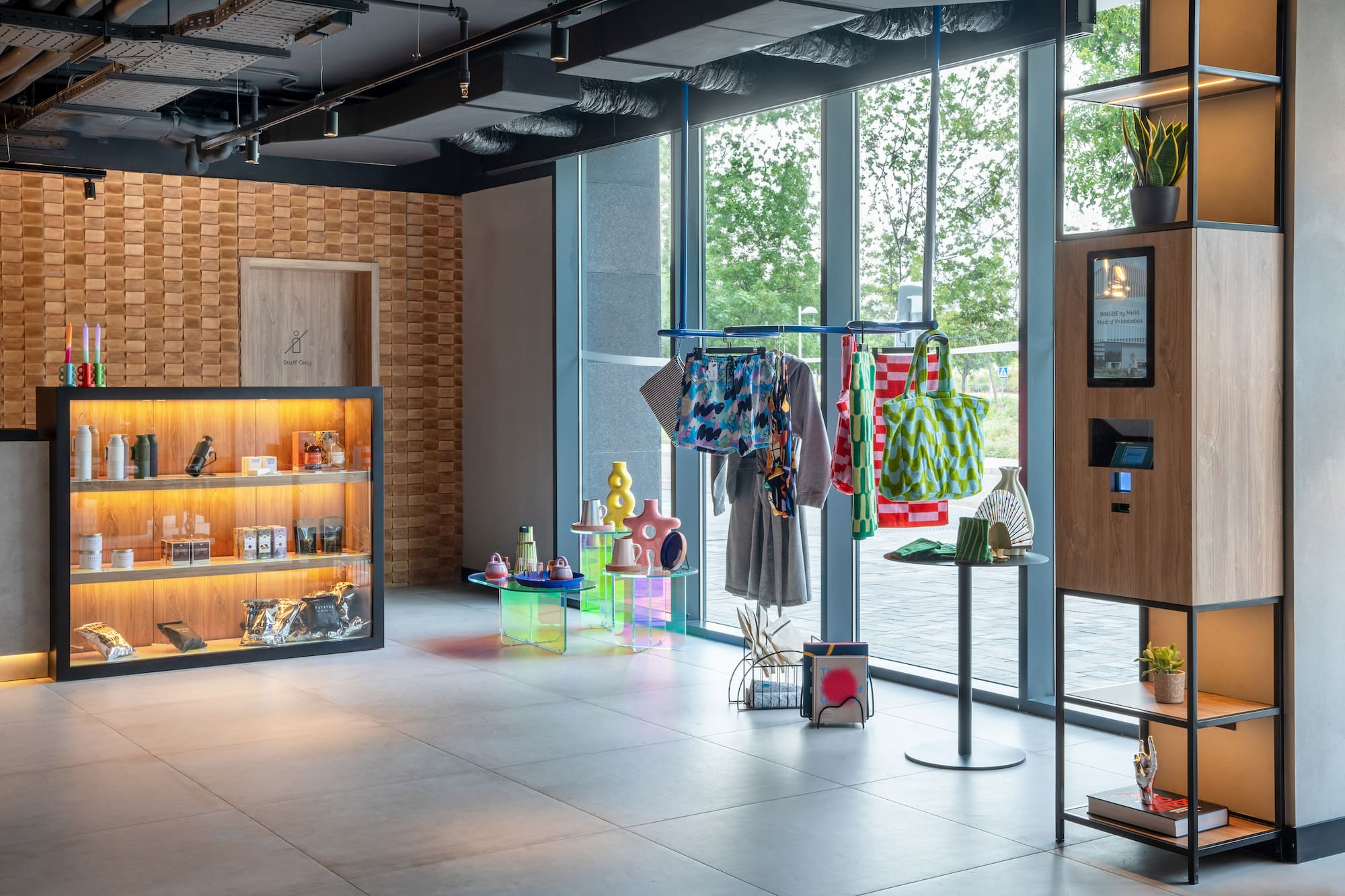 Modern hotel lobby with retail items, colorful clothing rack, and check-in kiosk.