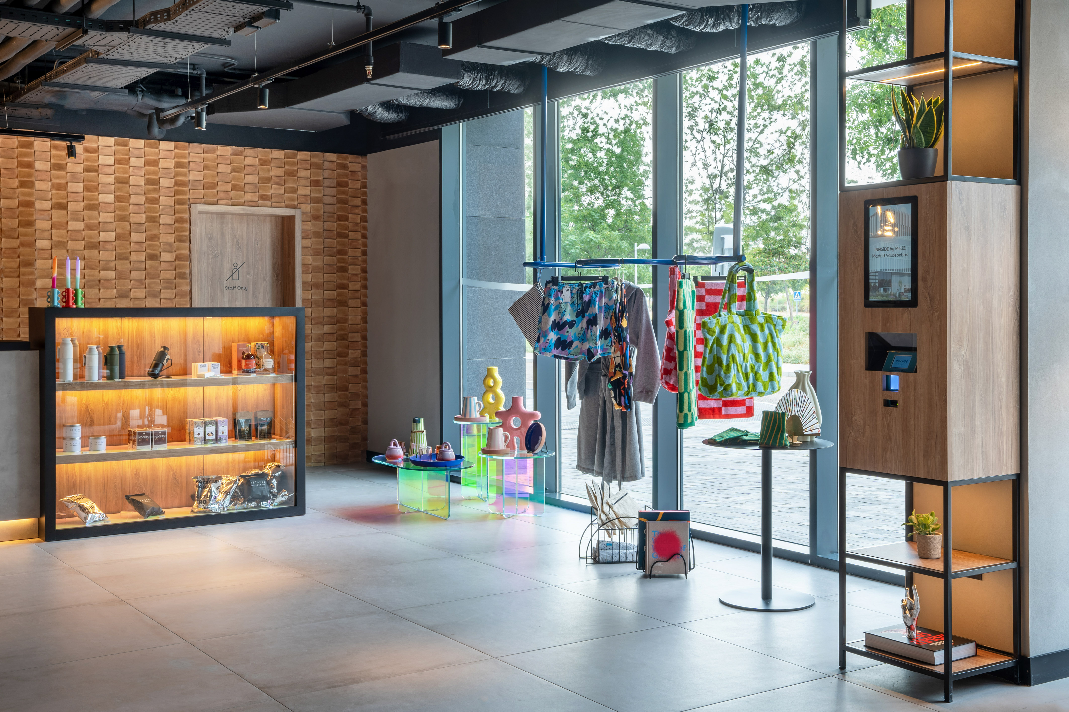 Modern hotel lobby with retail items, colorful clothing rack, and check-in kiosk.