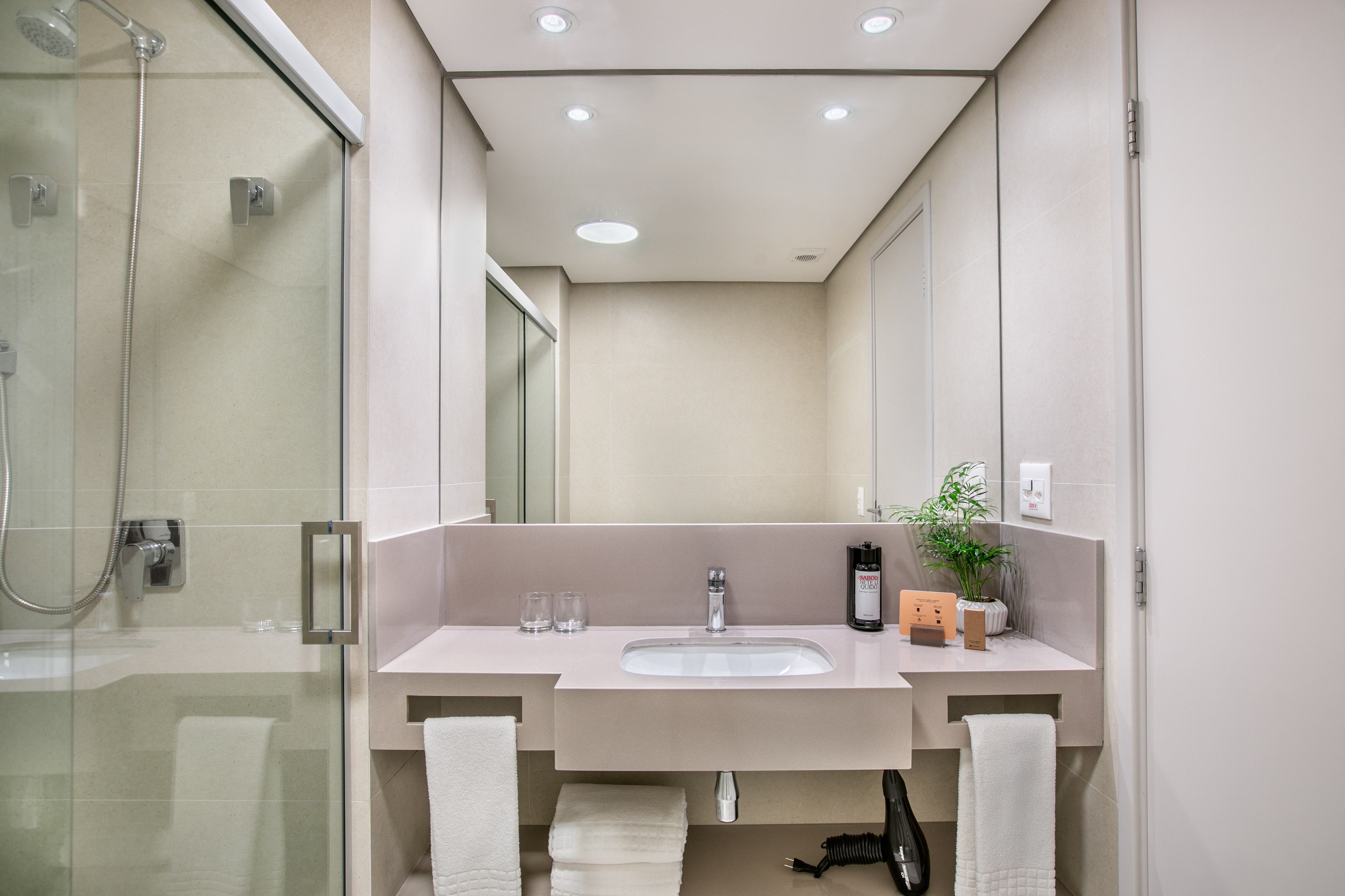 Sleek hotel bathroom with glass shower, modern vanity, sink, mirror, and towels.