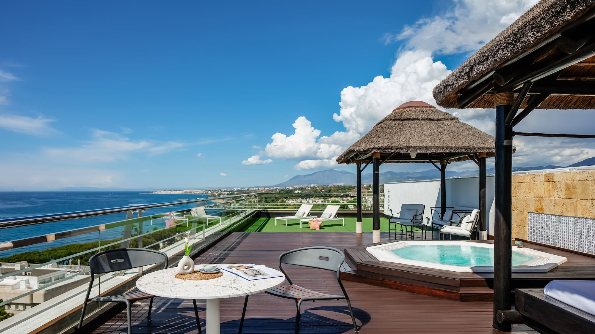 a deck with a hot tub and chairs and a thatched roof