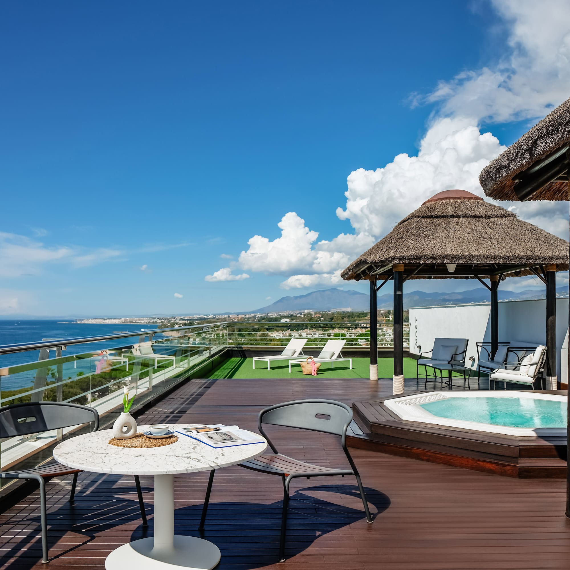 a deck with a hot tub and chairs and a thatched roof
