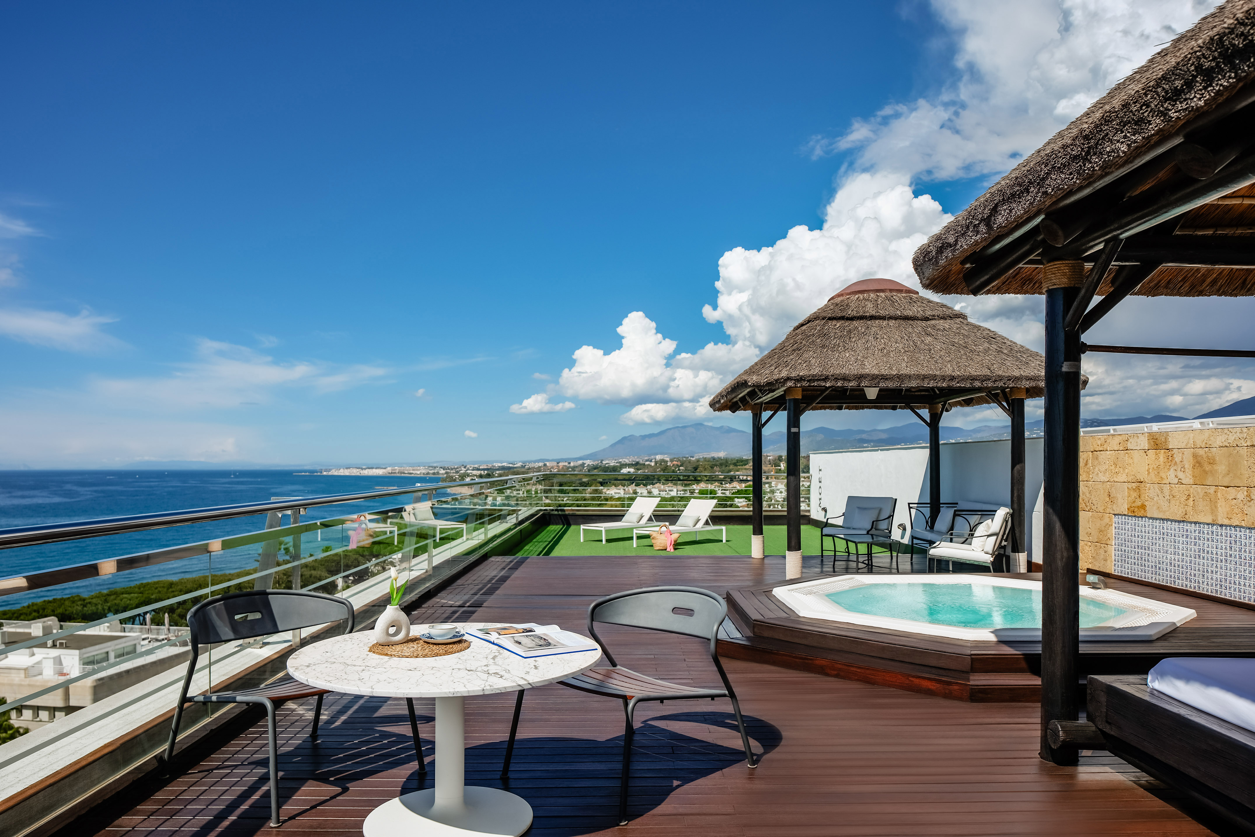 a deck with a hot tub and chairs and a thatched roof