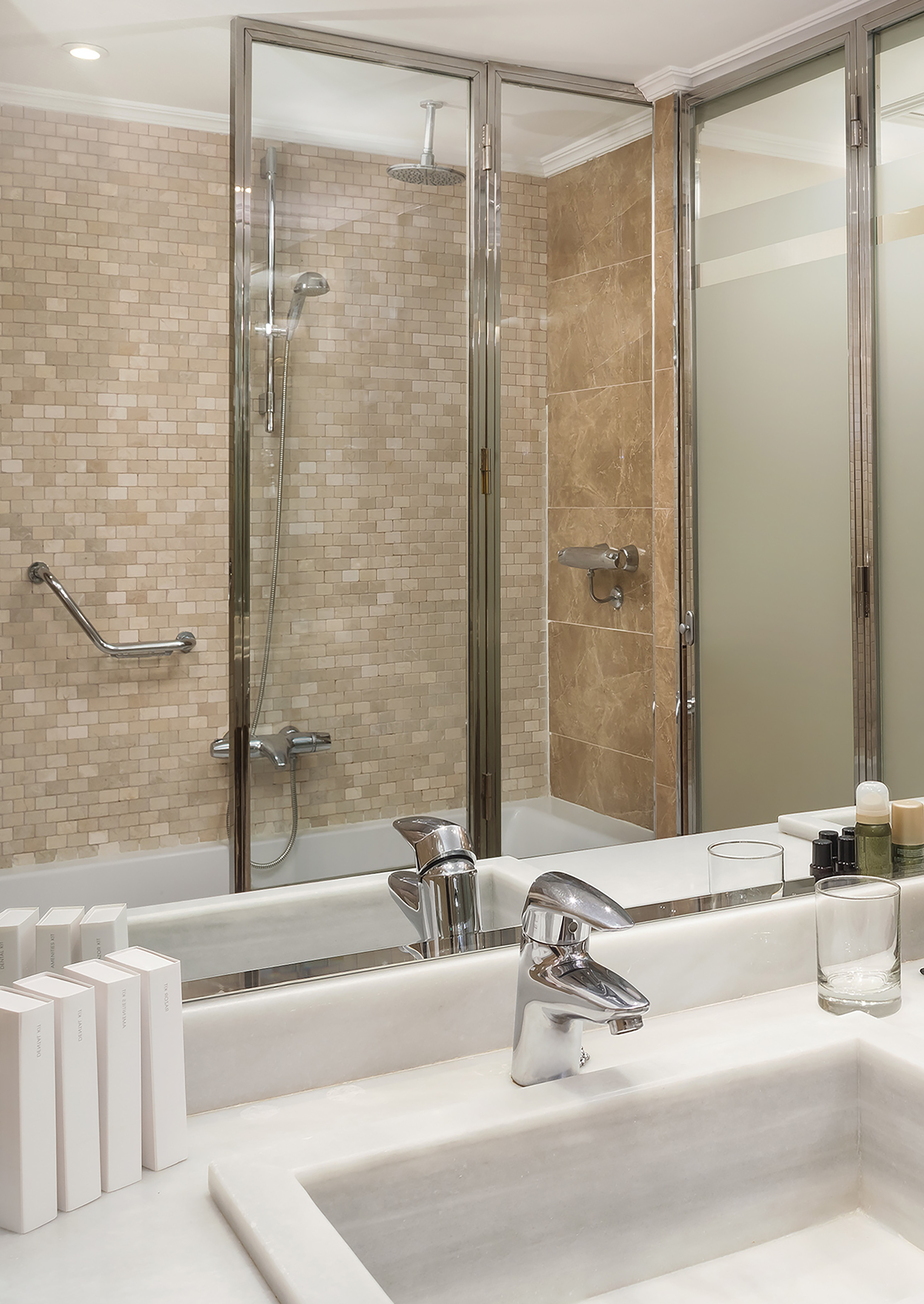 Marble vanity and sink in a modern bathroom with a mosaic tile shower.