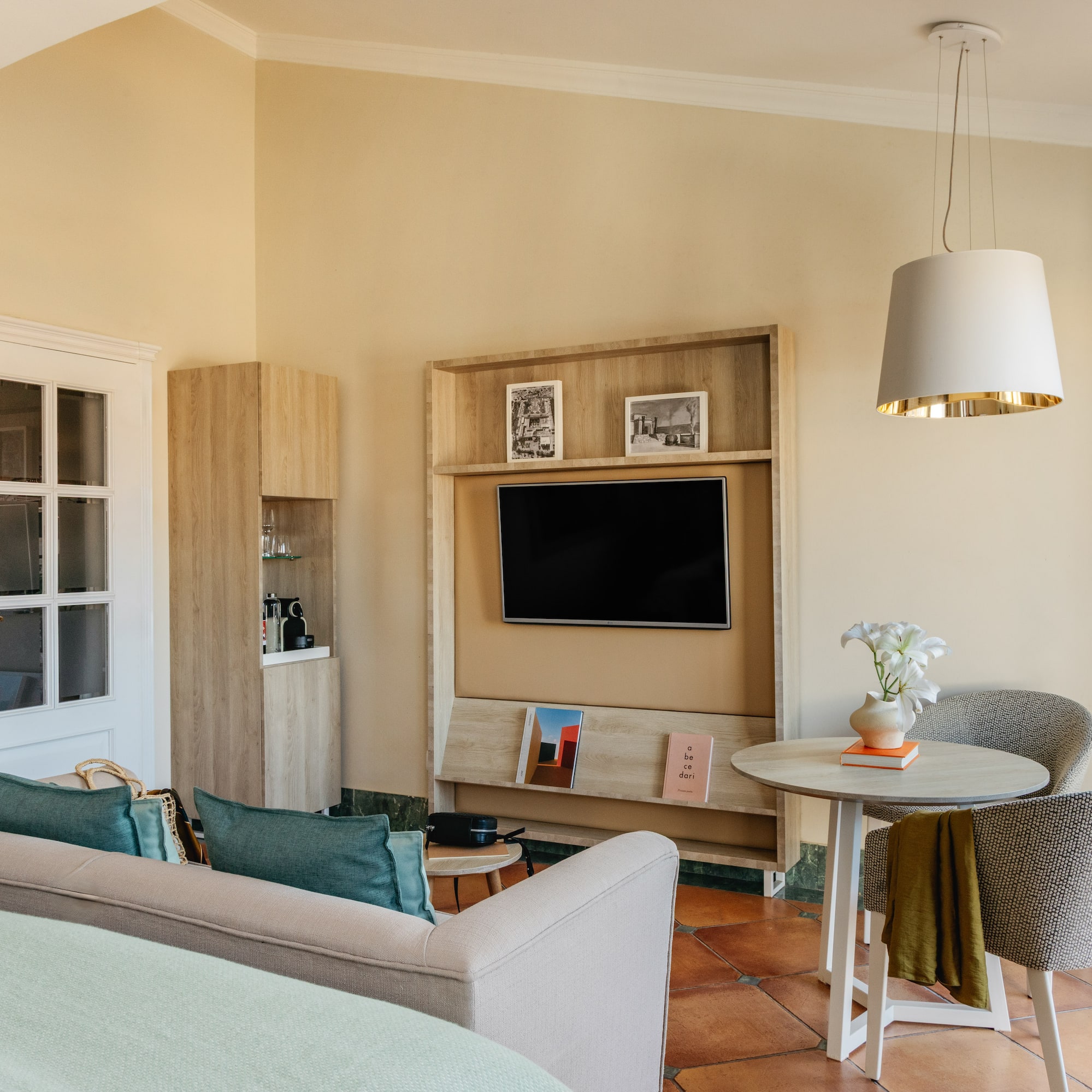 Modern hotel living area with sofa, wall-mounted TV, dining table, and warm decor.