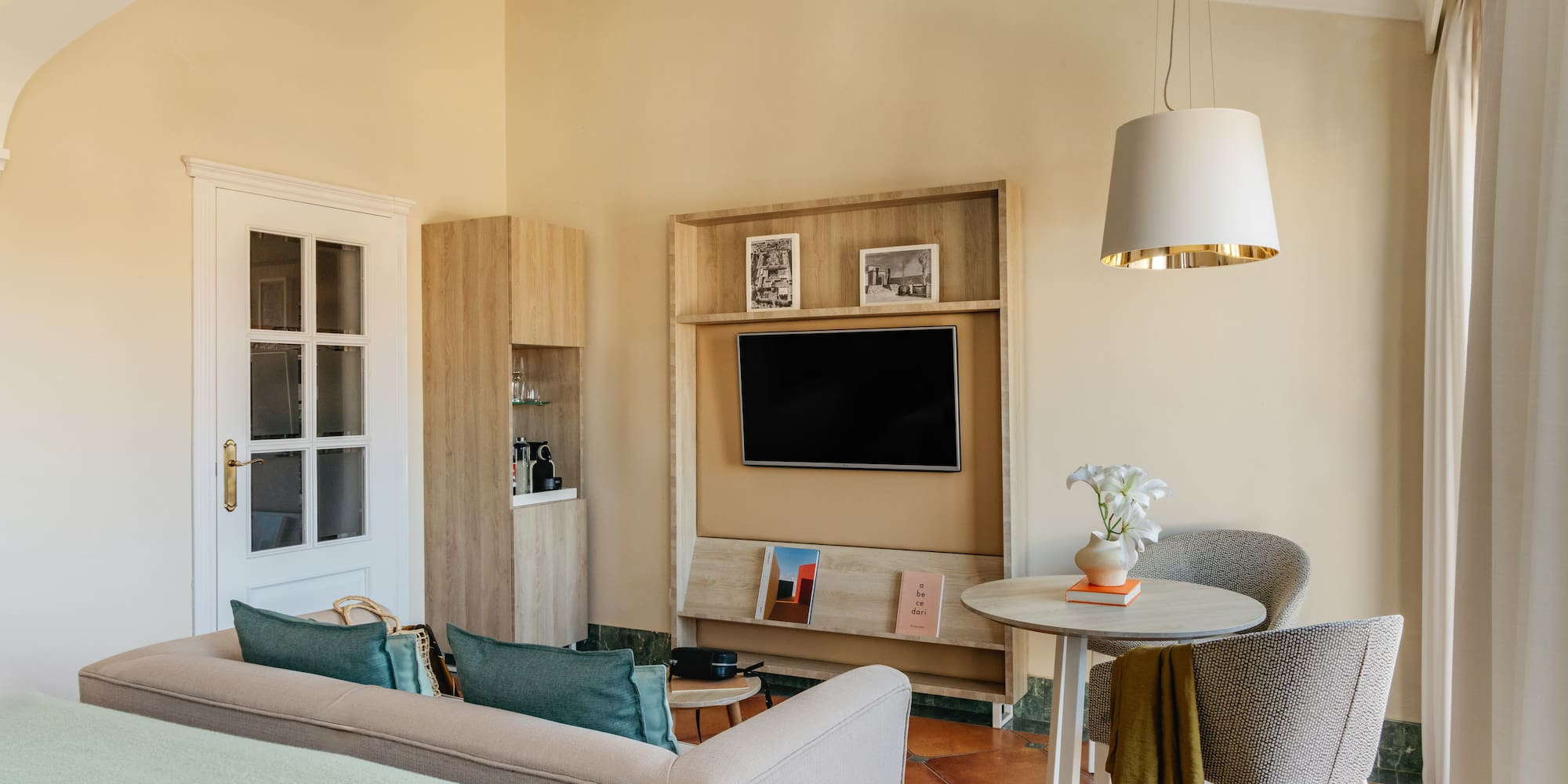 Modern hotel living area with sofa, wall-mounted TV, dining table, and warm decor.