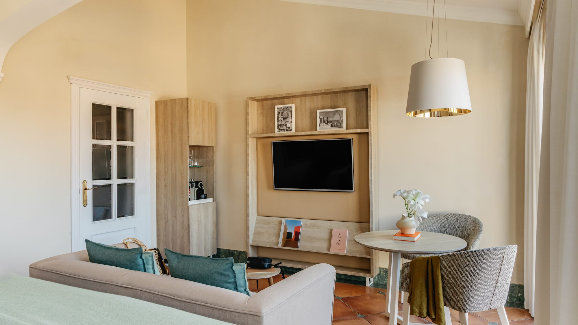 Modern hotel living area with sofa, wall-mounted TV, dining table, and warm decor.
