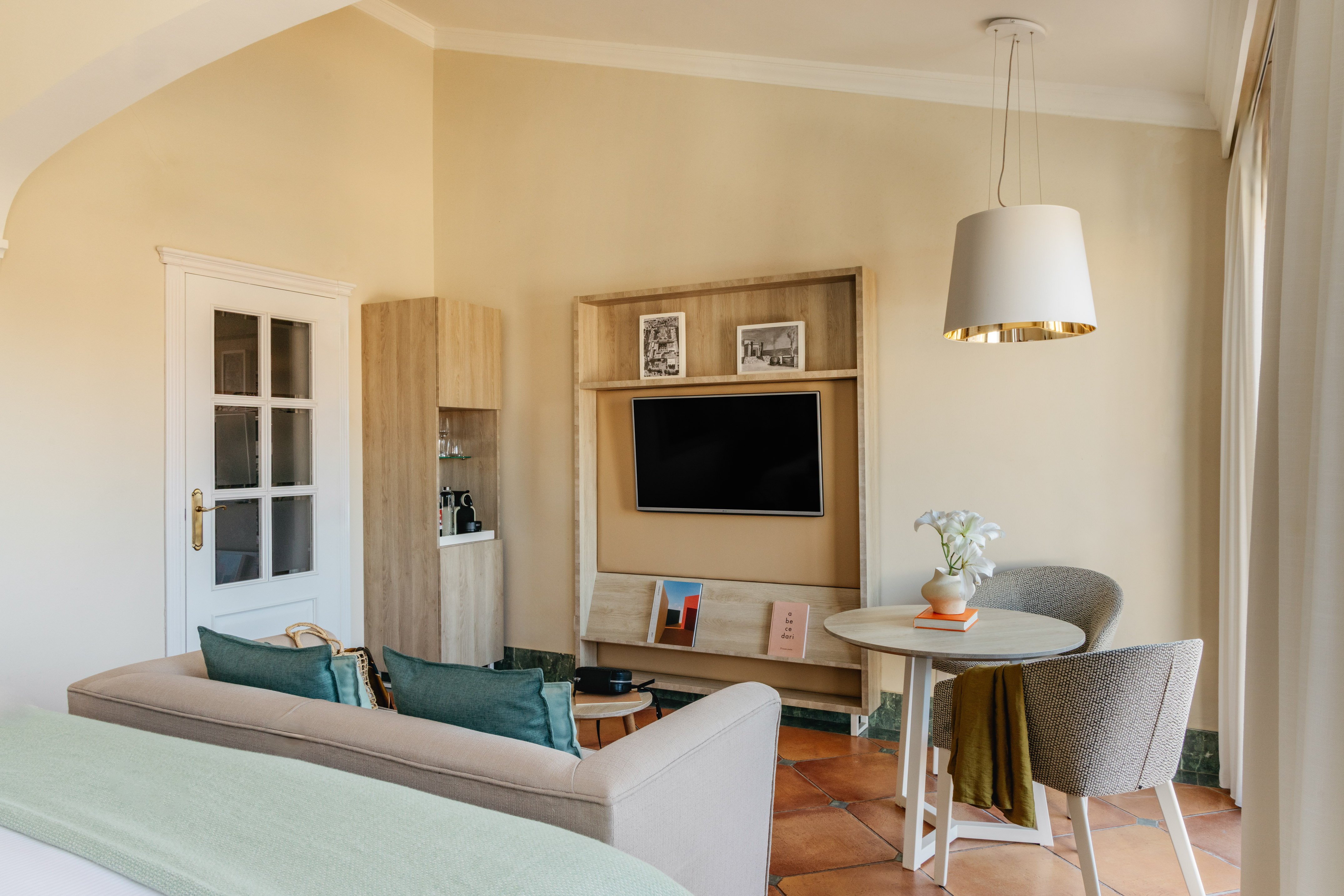 Modern hotel living area with sofa, wall-mounted TV, dining table, and warm decor.