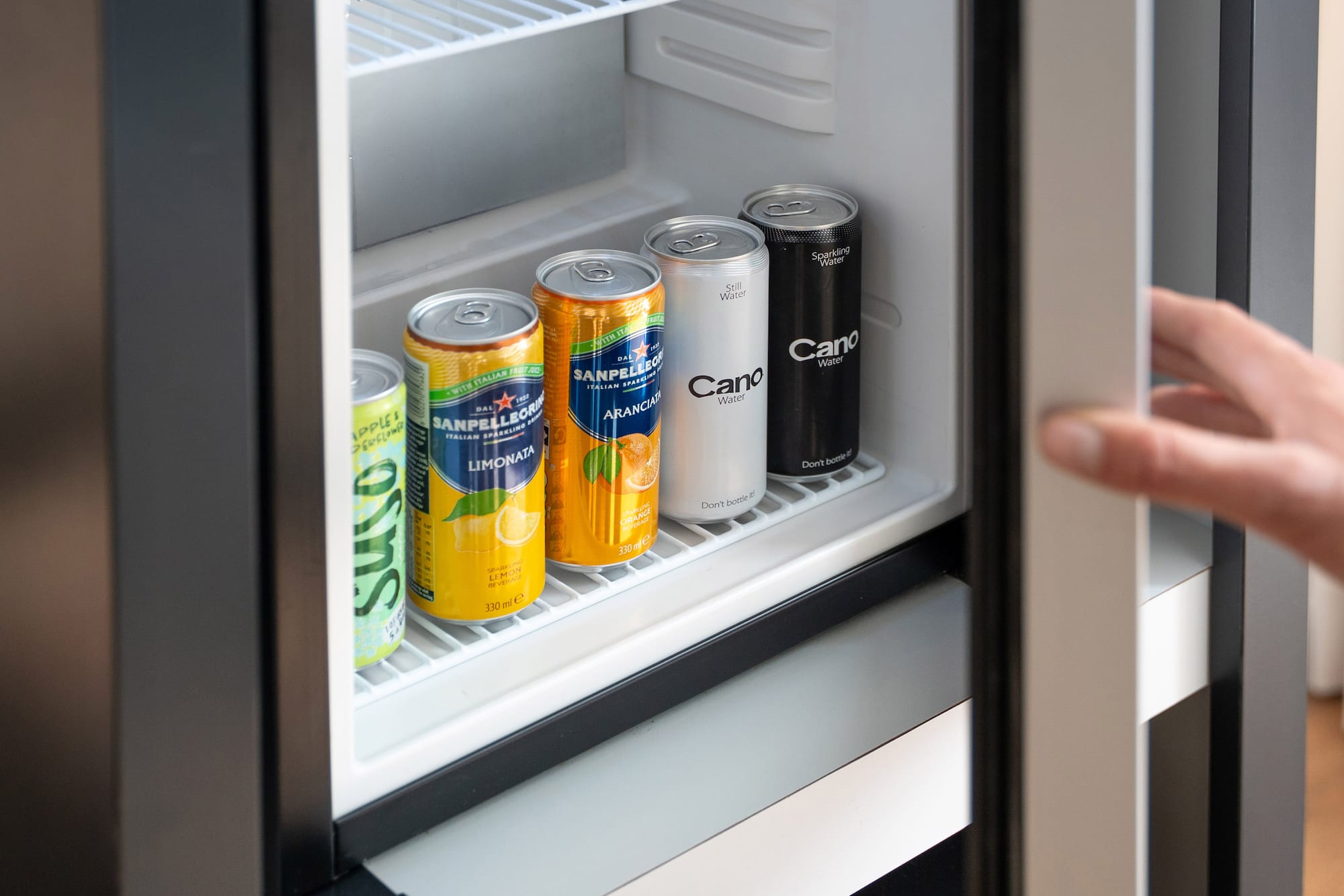 Mini-fridge with San Pellegrino, Cano Water cans. Hand opening door.