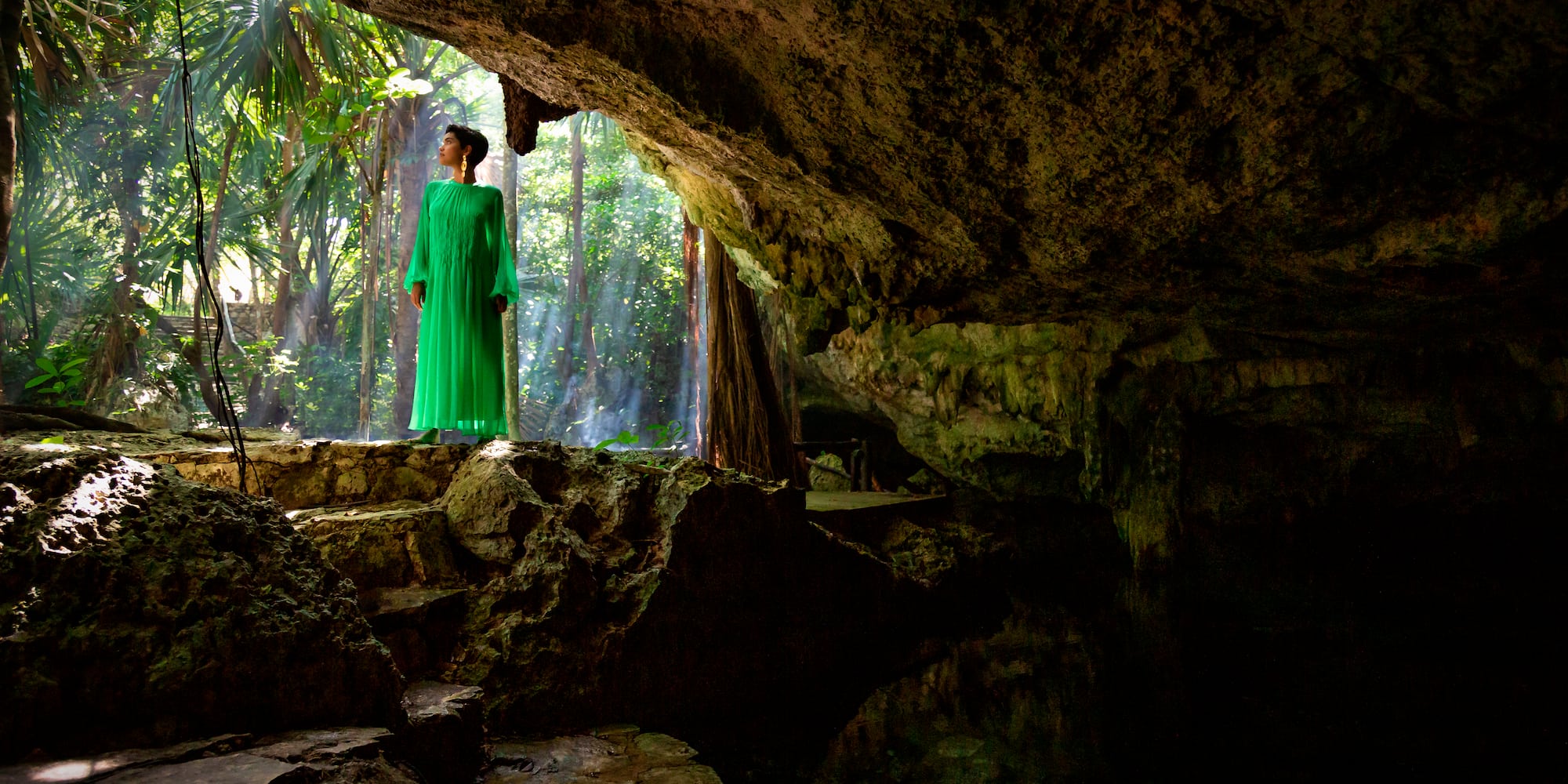 a woman in a green dress standing in a cave