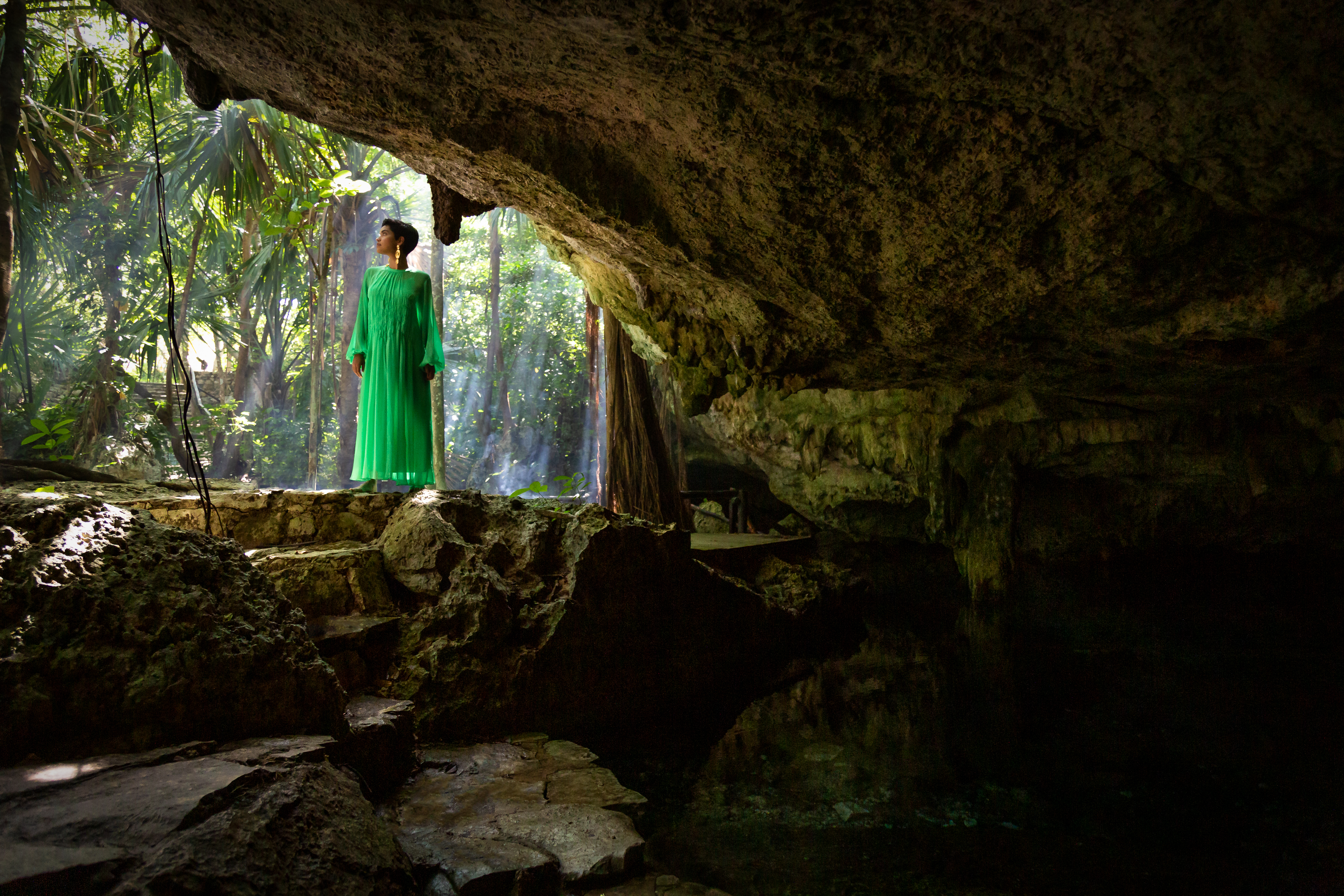 a woman in a green dress standing in a cave