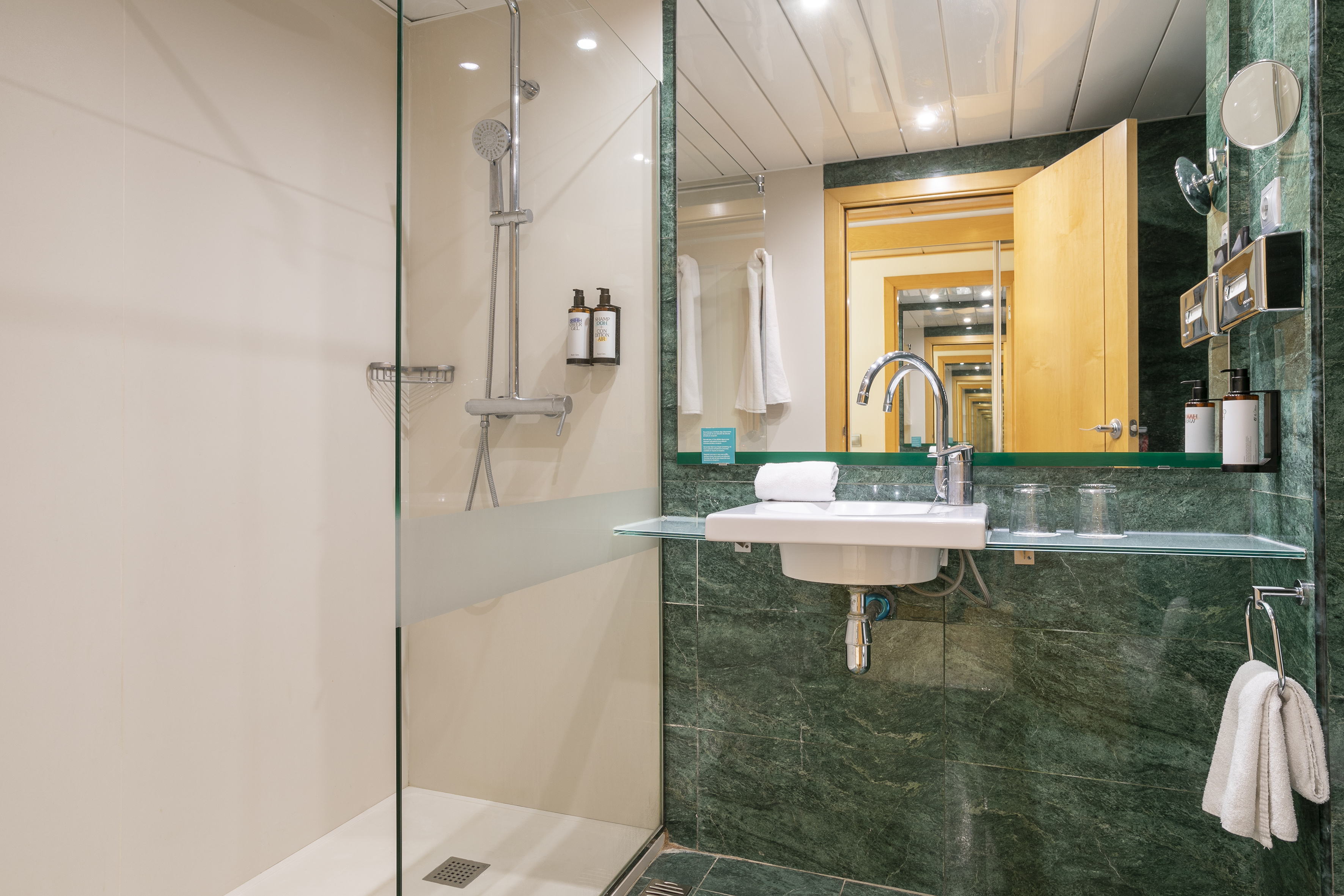 Modern hotel bathroom with green marble walls, glass shower, and vanity sink.