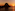 Sunset over ocean with dark rocky island silhouette, reflecting orange sky.