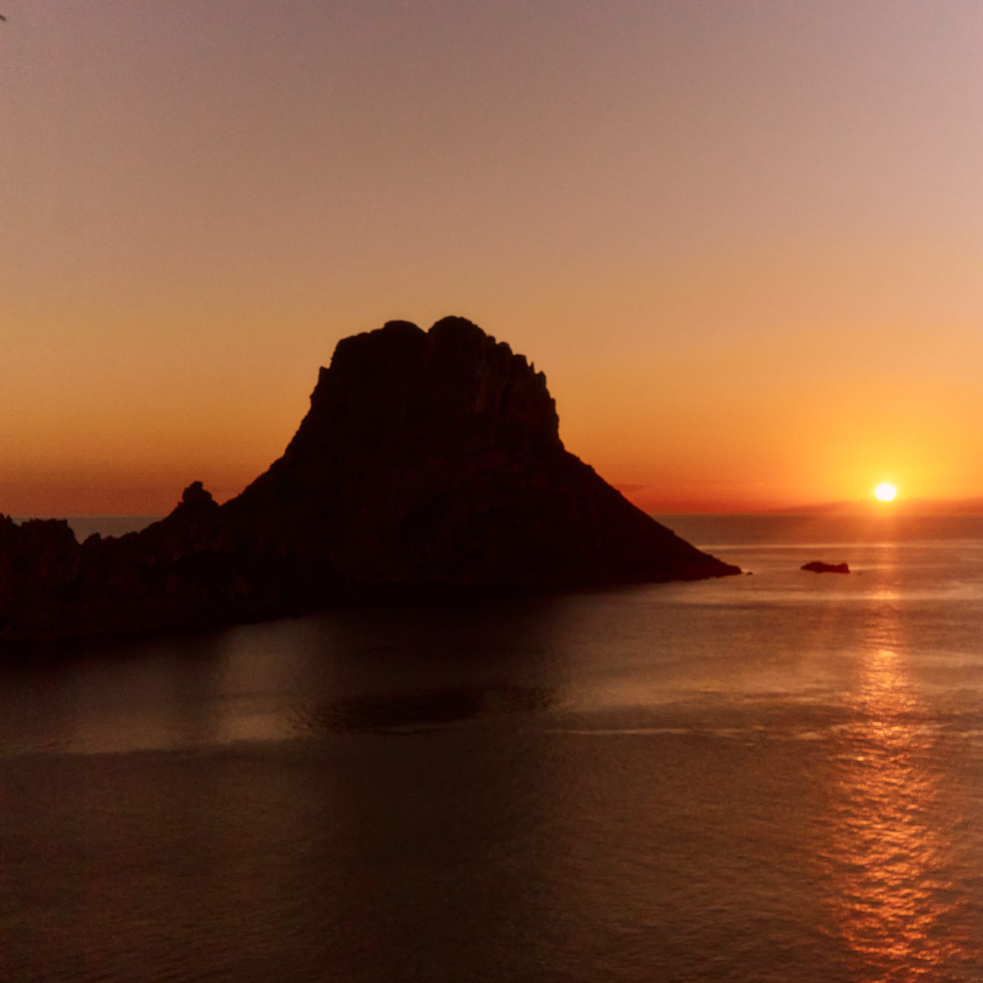 Es Vedra island silhouette at sunset over the Mediterranean Sea.