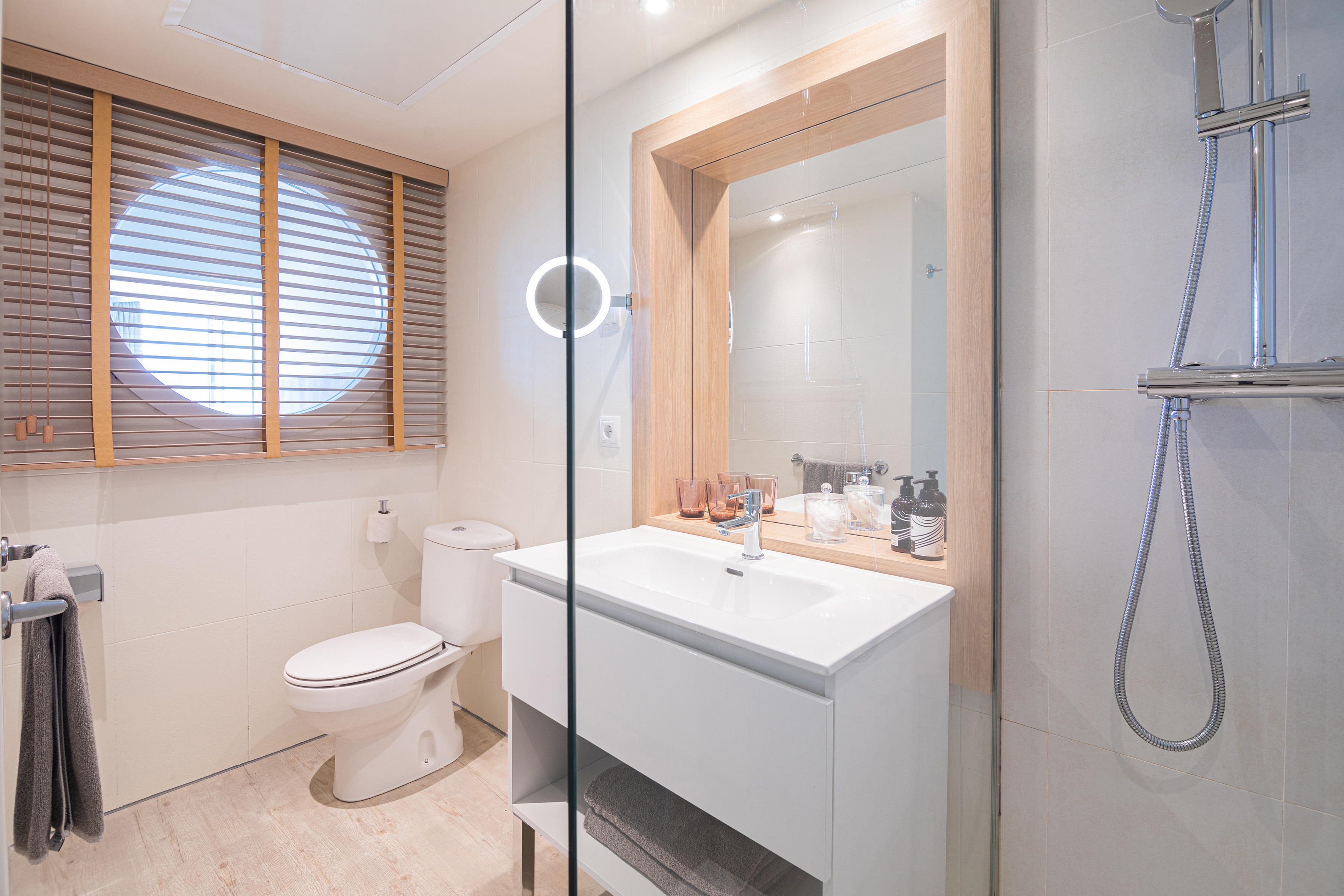 Modern bathroom with white vanity, toilet, glass shower, round window blinds.