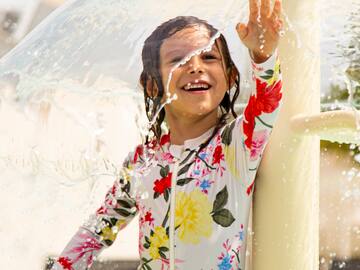 a girl in a wet suit under a water fountain