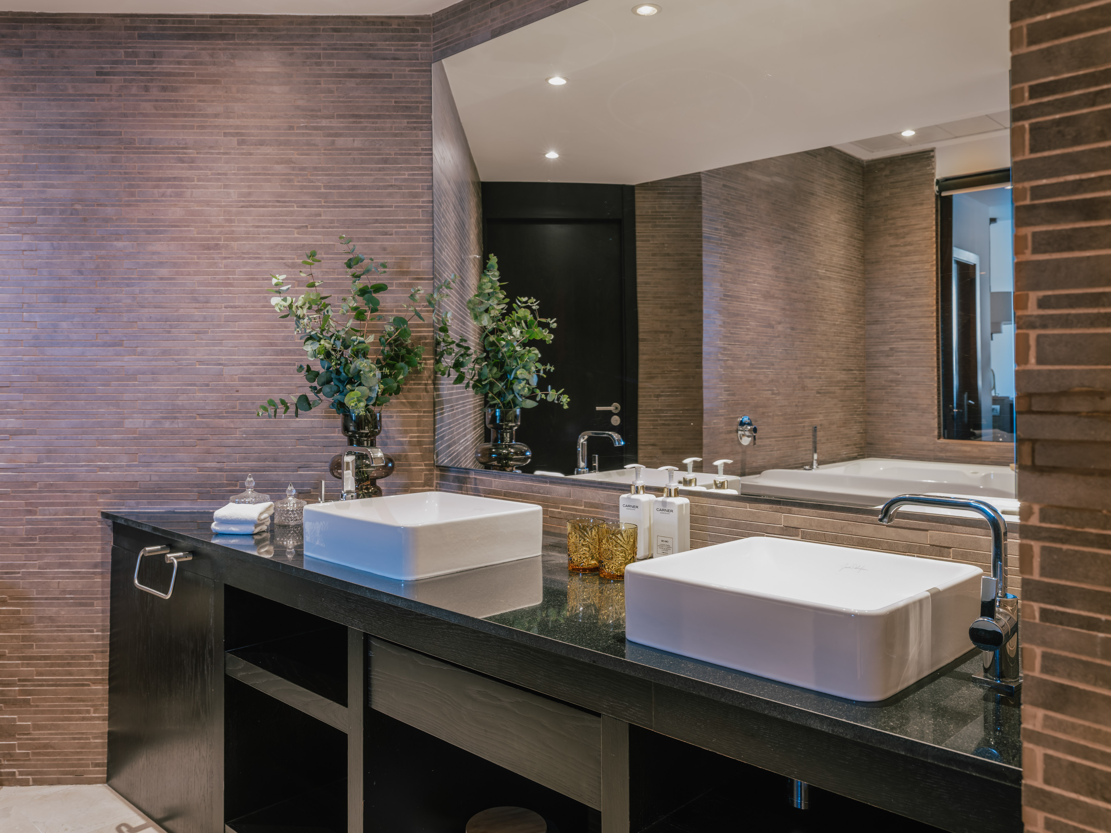 Modern bathroom with double vanity, white vessel sinks, and textured wall tiles.