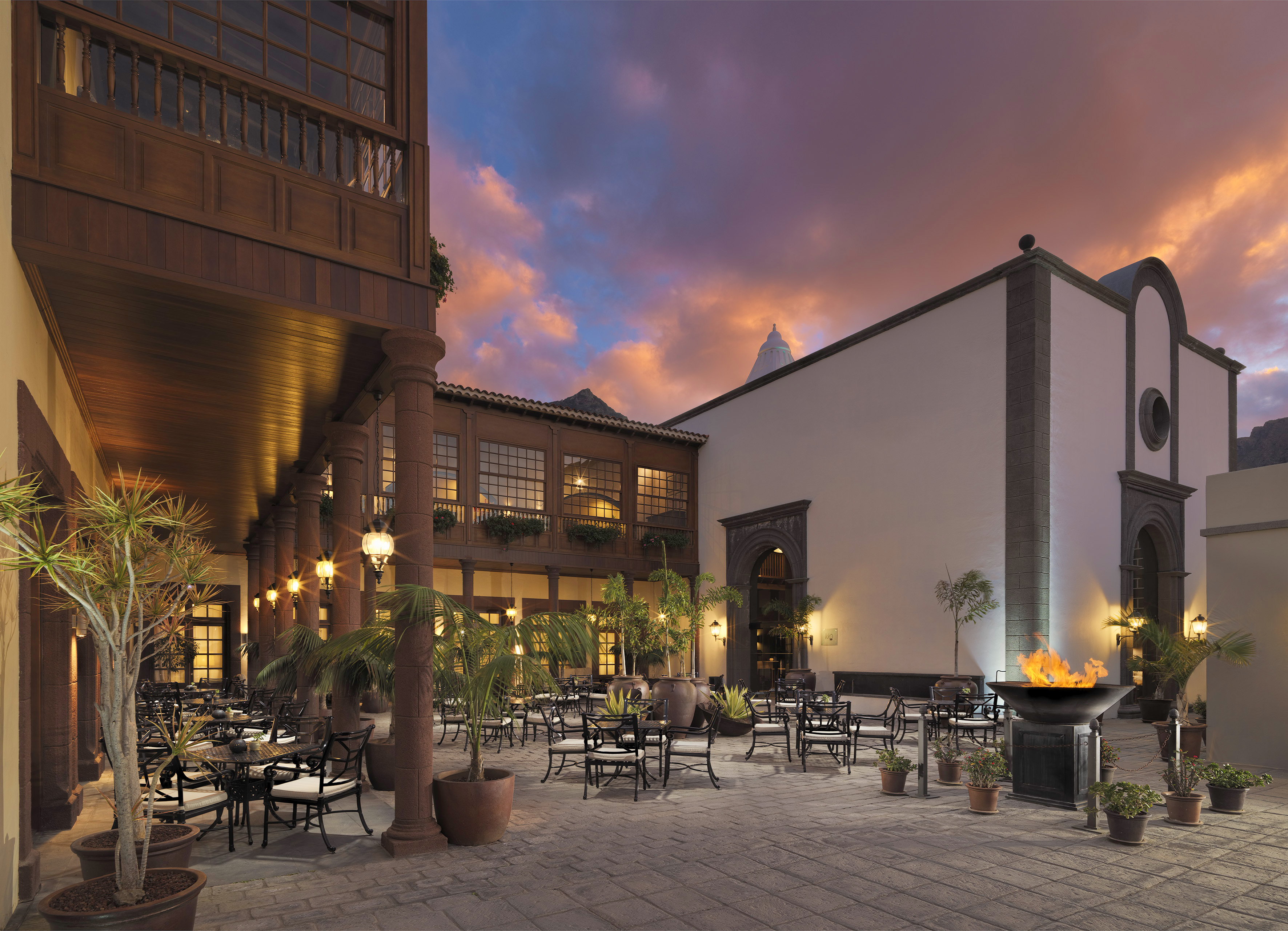 Resort courtyard with fire pit, outdoor dining tables, and colorful sunset sky.