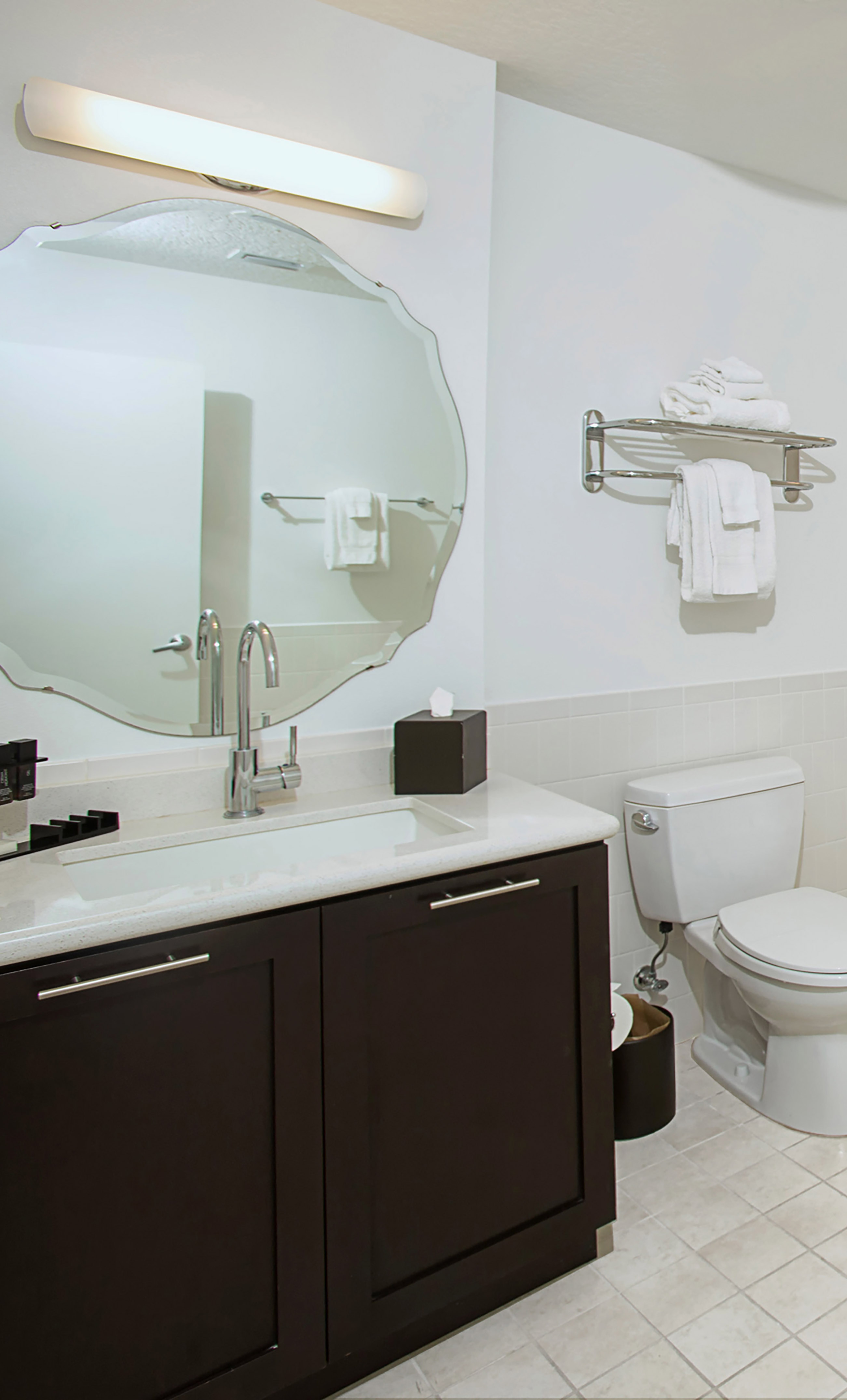 Contemporary hotel bathroom with dark vanity, white sink, unique mirror, toilet. - One-Bedroom Suite 2 Queen Beds - Meliá Orlando Celebration, Orlando