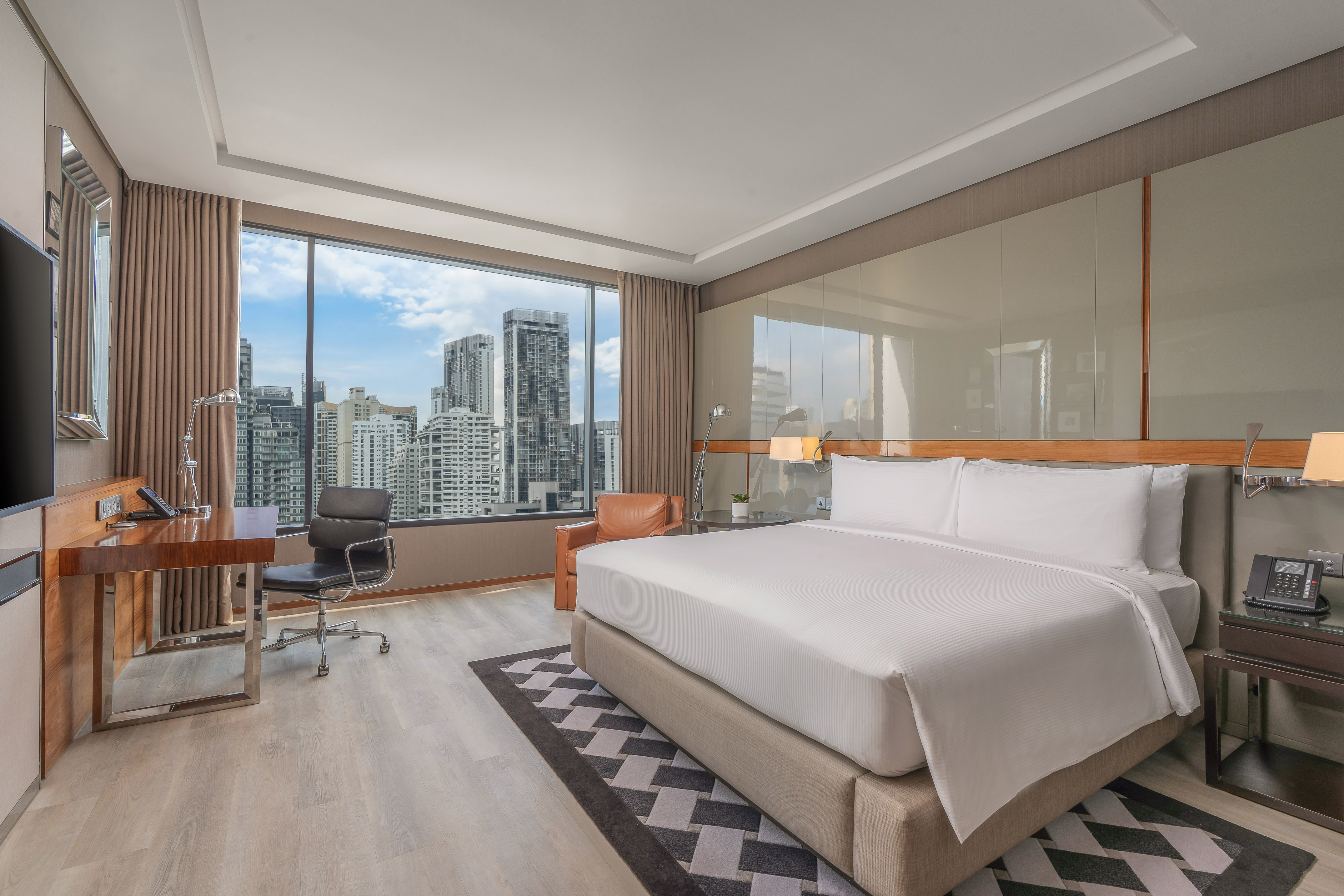 Modern hotel bedroom with large bed, work desk, and a city skyline view.