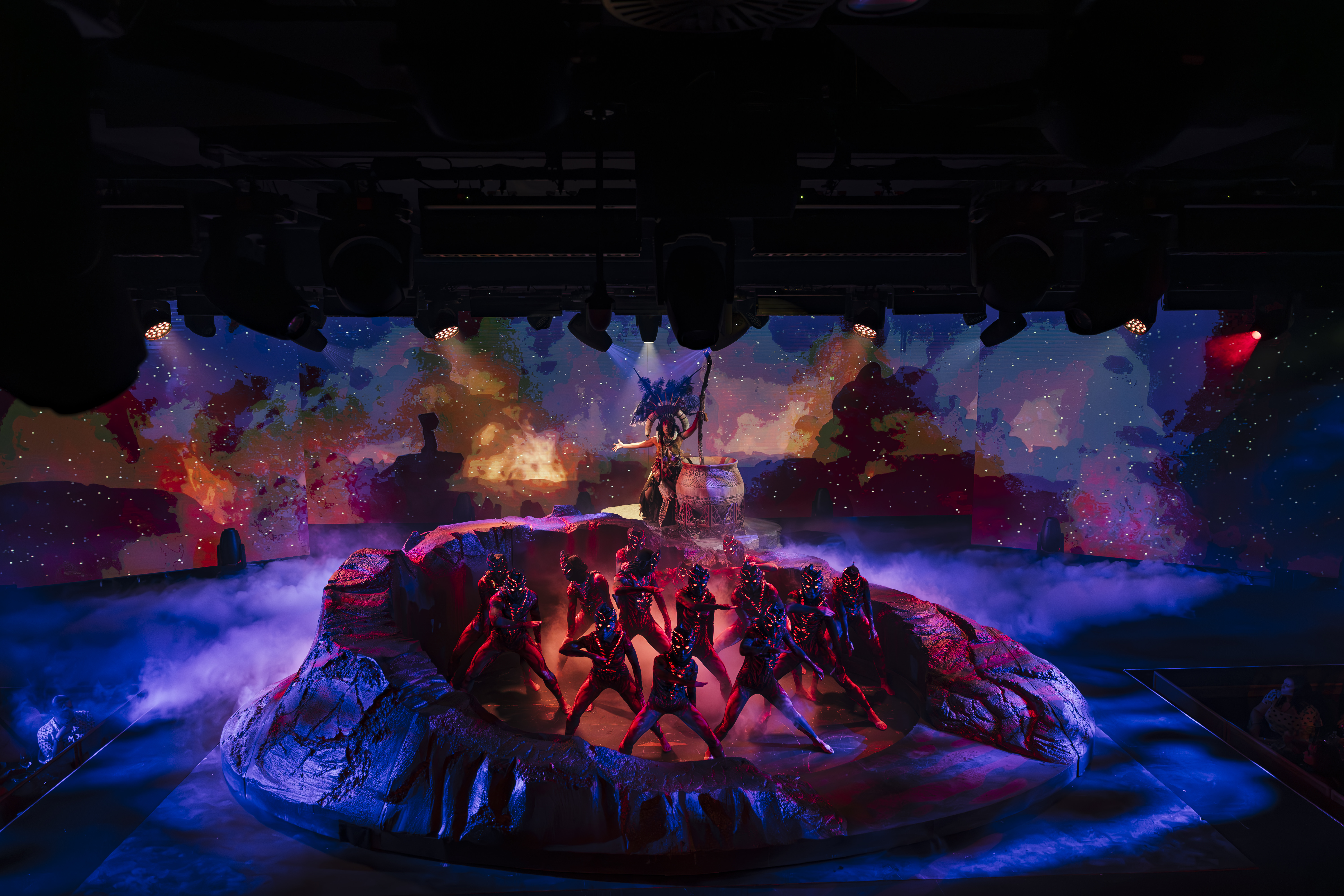 Theatrical tribal show with dancers, cosmic backdrop, and smoky stage.