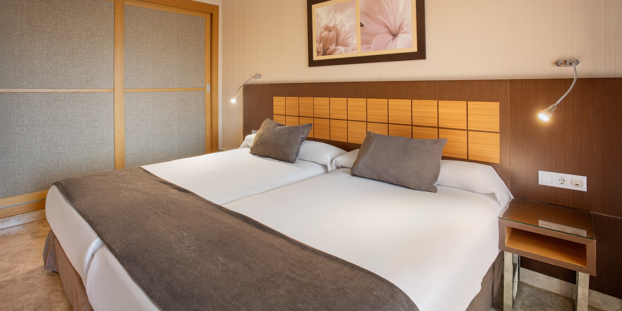 Modern hotel room with twin beds, brown headboard, and sliding wardrobe.