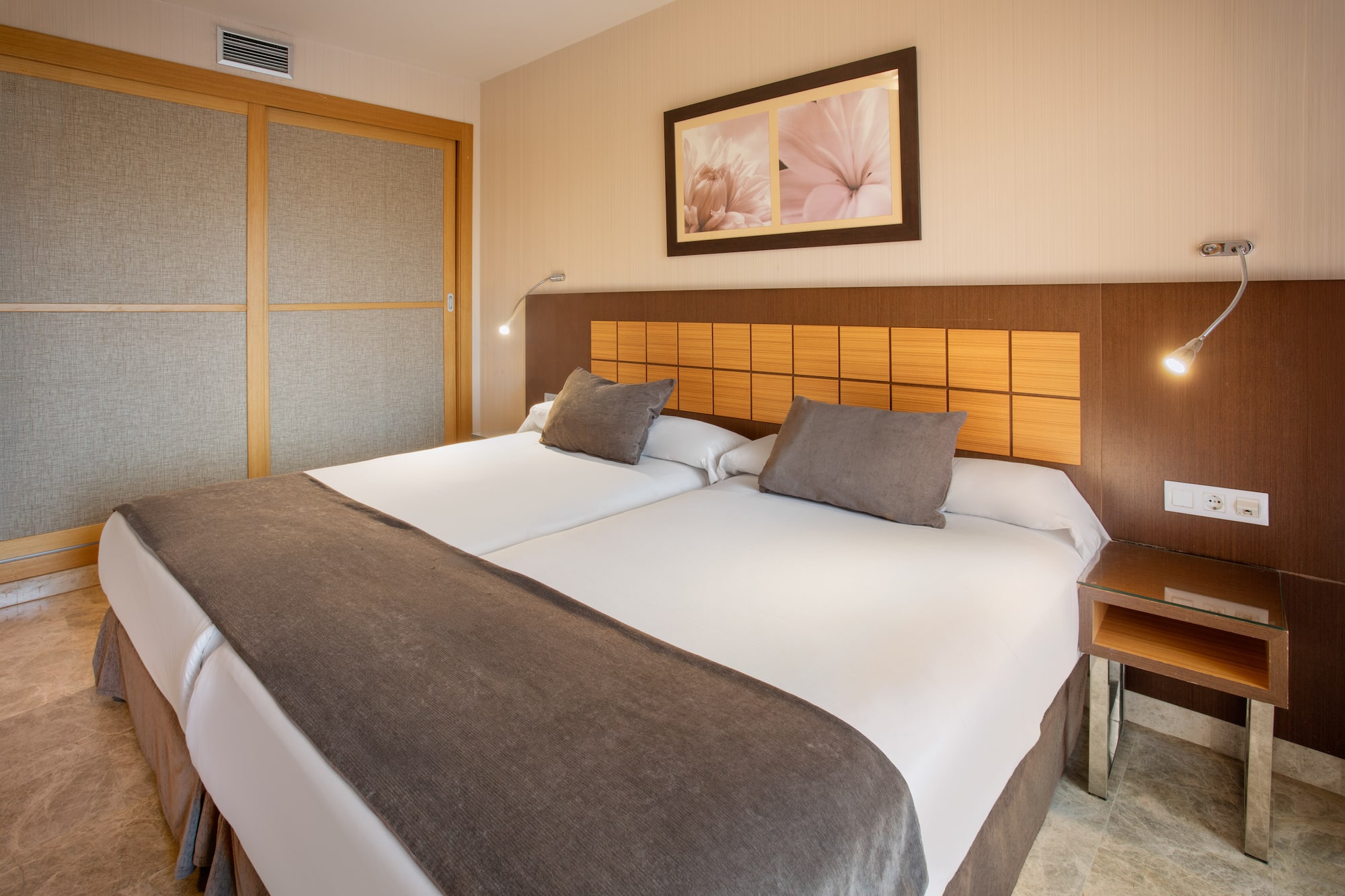 Modern hotel room with twin beds, wooden headboard, bedside lamps, and closet.