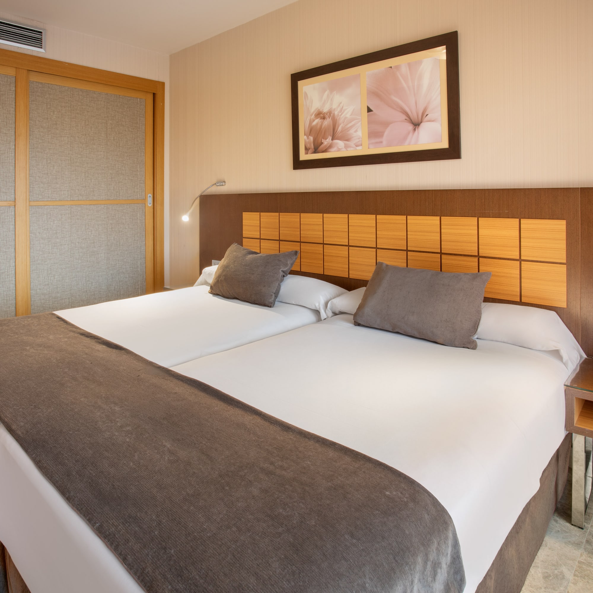 Modern hotel room with twin beds, brown headboard, and sliding wardrobe.