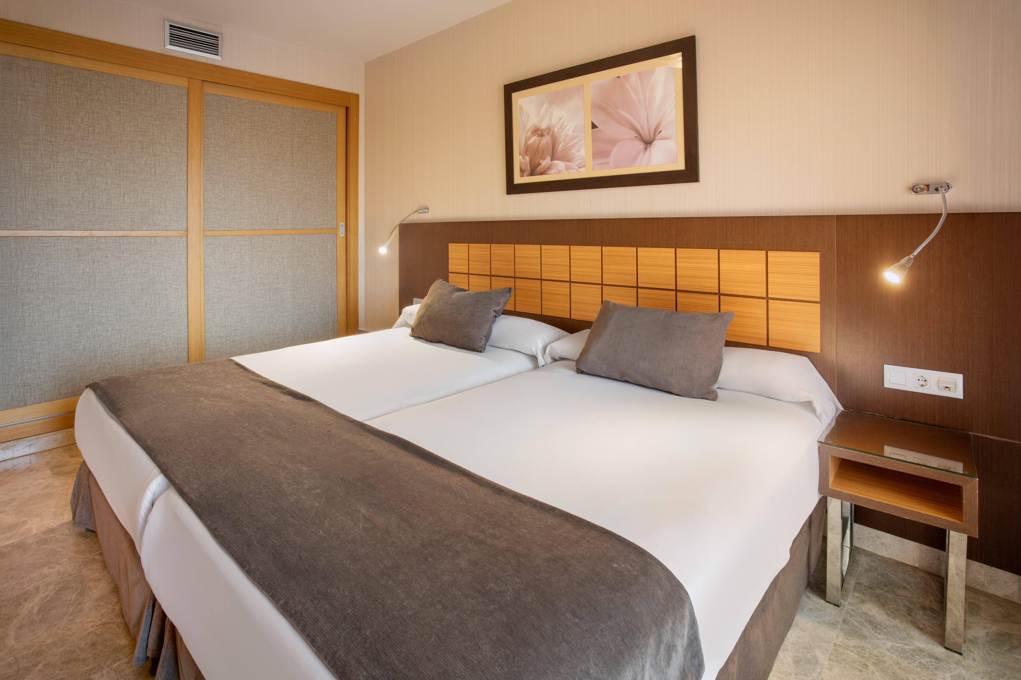Modern hotel room with twin beds, wooden headboard, bedside lamps, and closet.