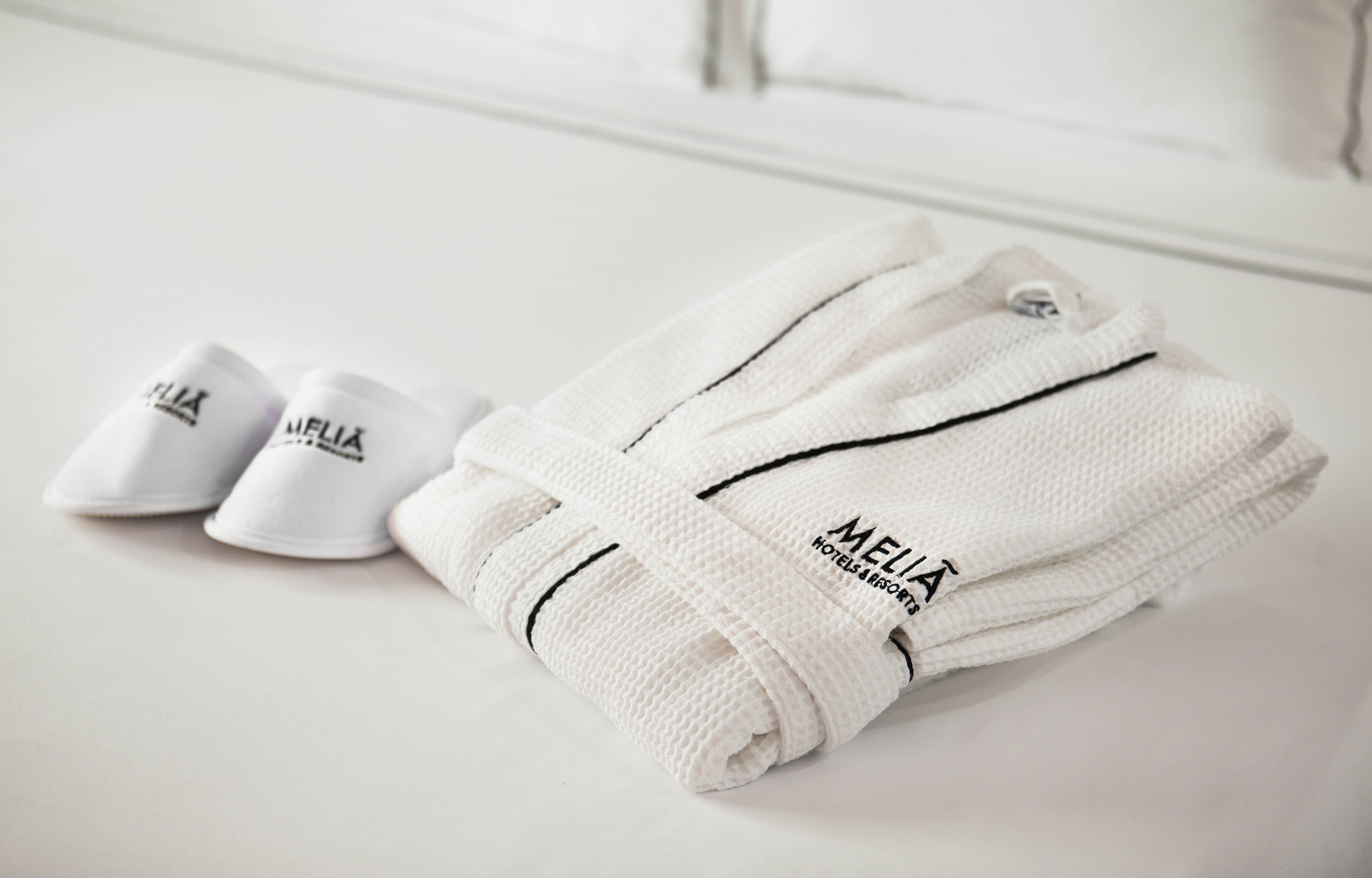 Meliá Hotels & Resorts white waffle bathrobe and slippers on a hotel bed.