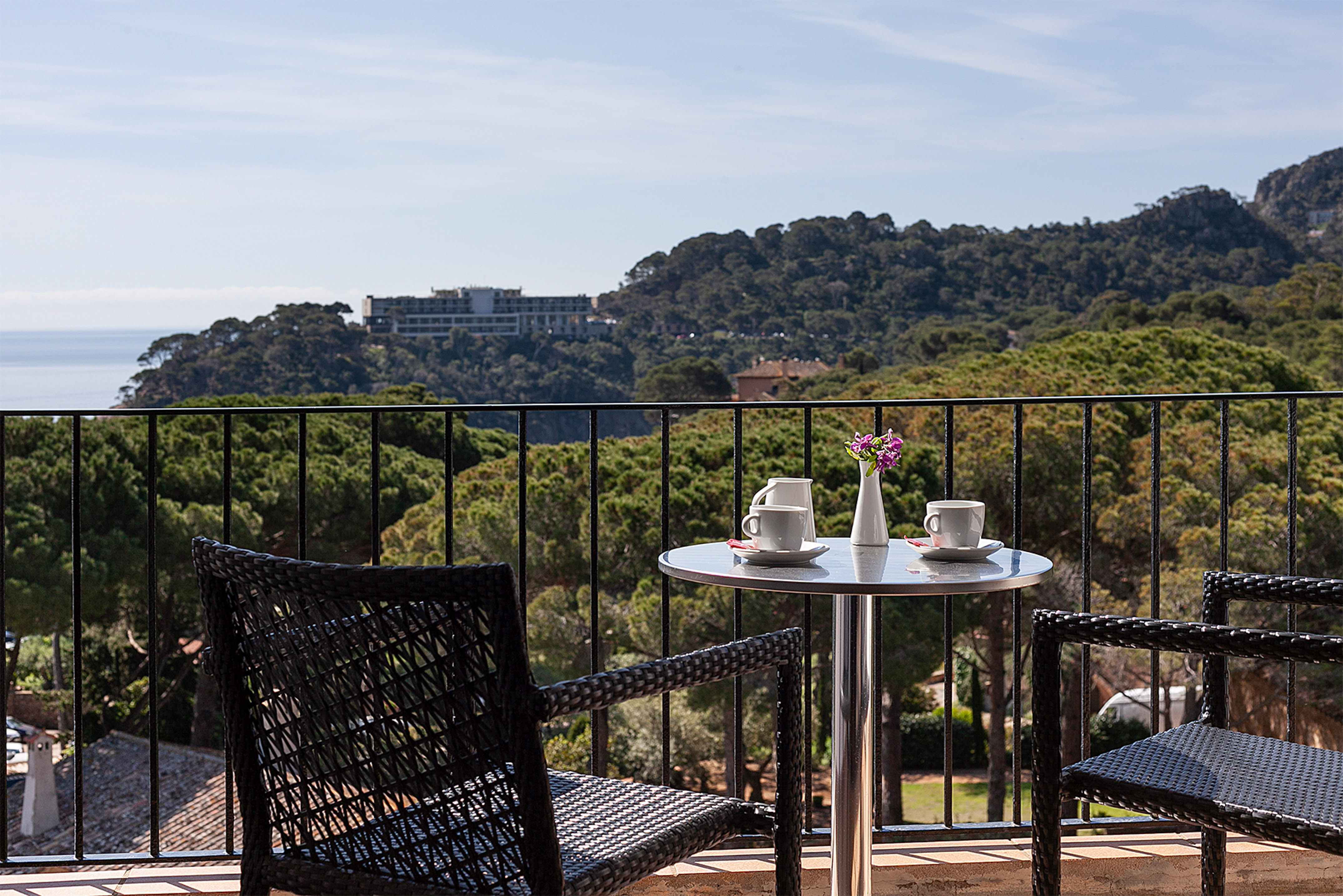 Balcony with coffee on table, chairs, overlooking sea and forest.