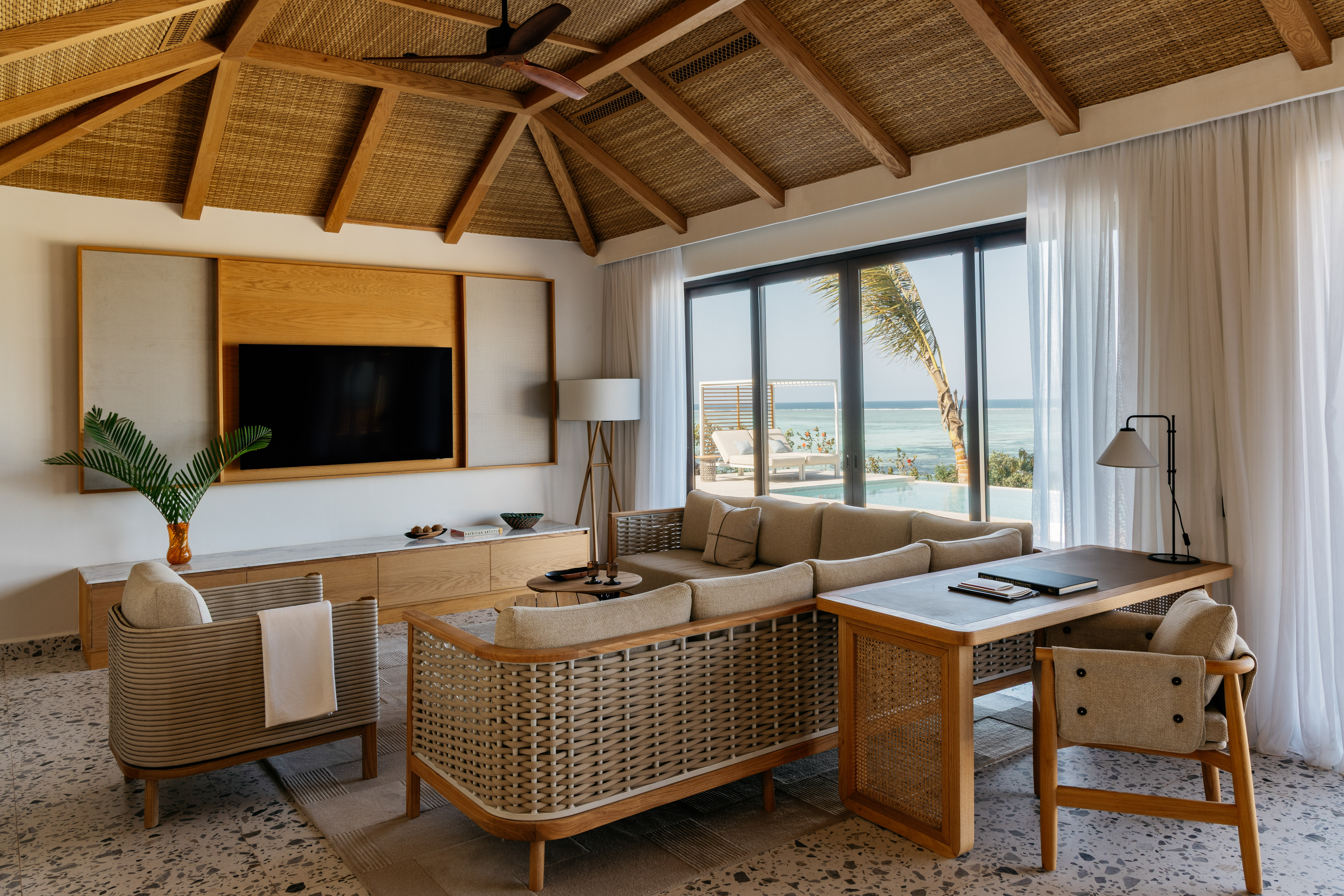 Tropical luxury living room with ocean view, woven furniture, and thatched ceiling.