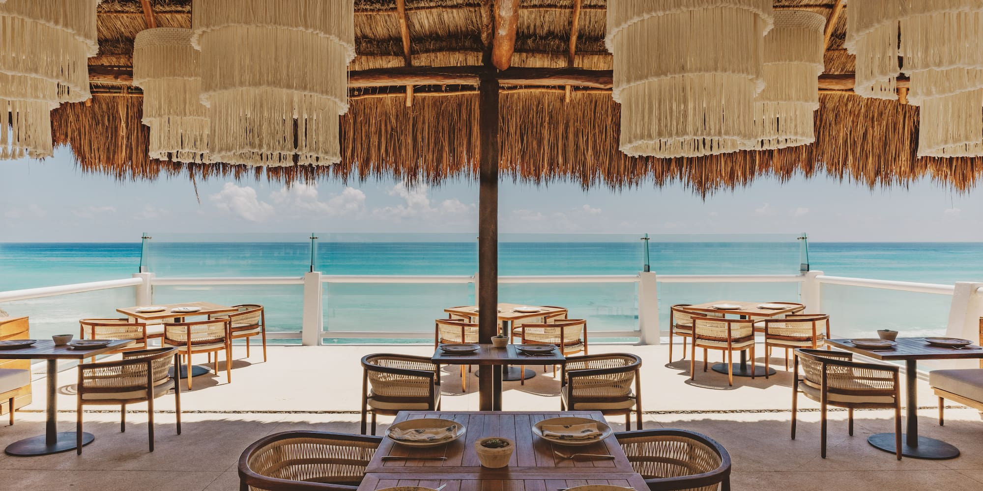 Tropical restaurant with ocean views, thatched roof, and macrame chandeliers.