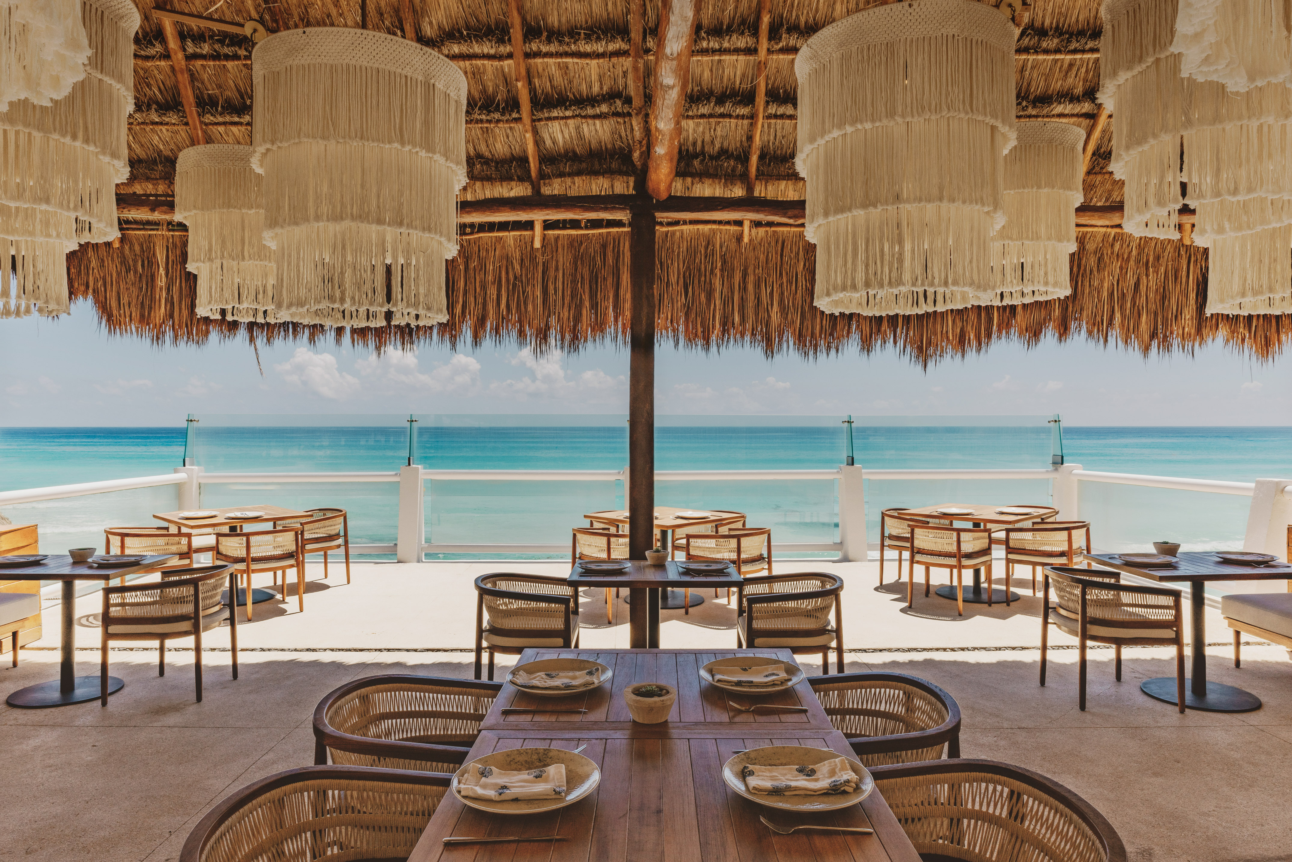 Tropical restaurant with ocean views, thatched roof, and macrame chandeliers.
