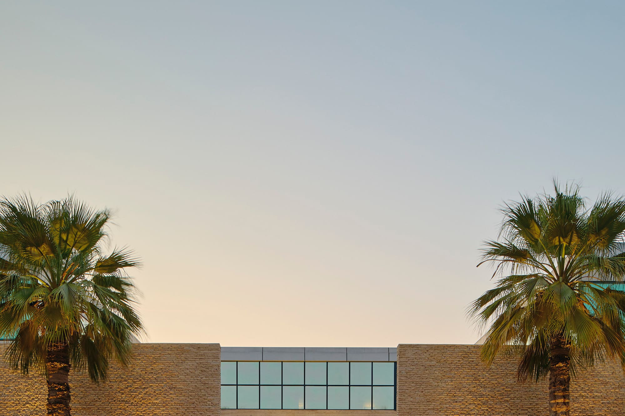Modern hotel entrance, illuminated steps, palm trees, and abstract sculpture.