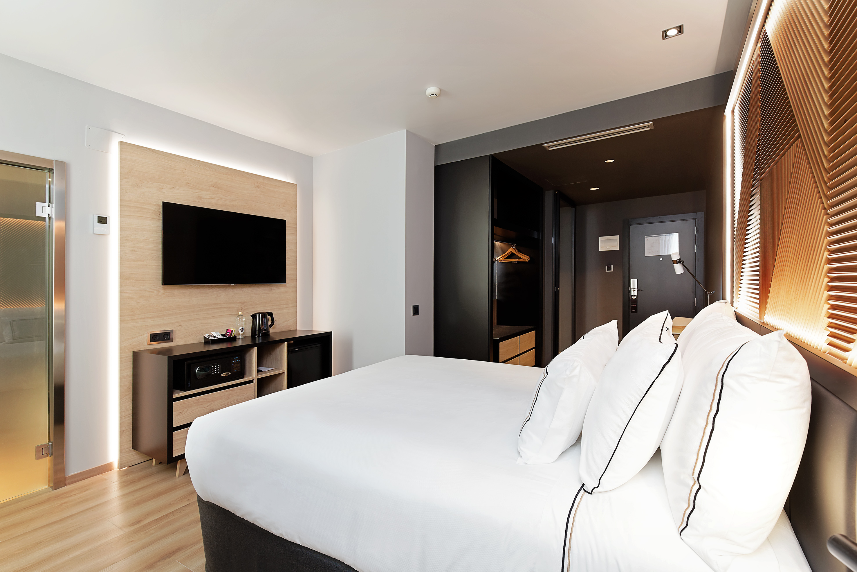 Modern hotel bedroom with large bed, wall-mounted TV, and minimalist design.