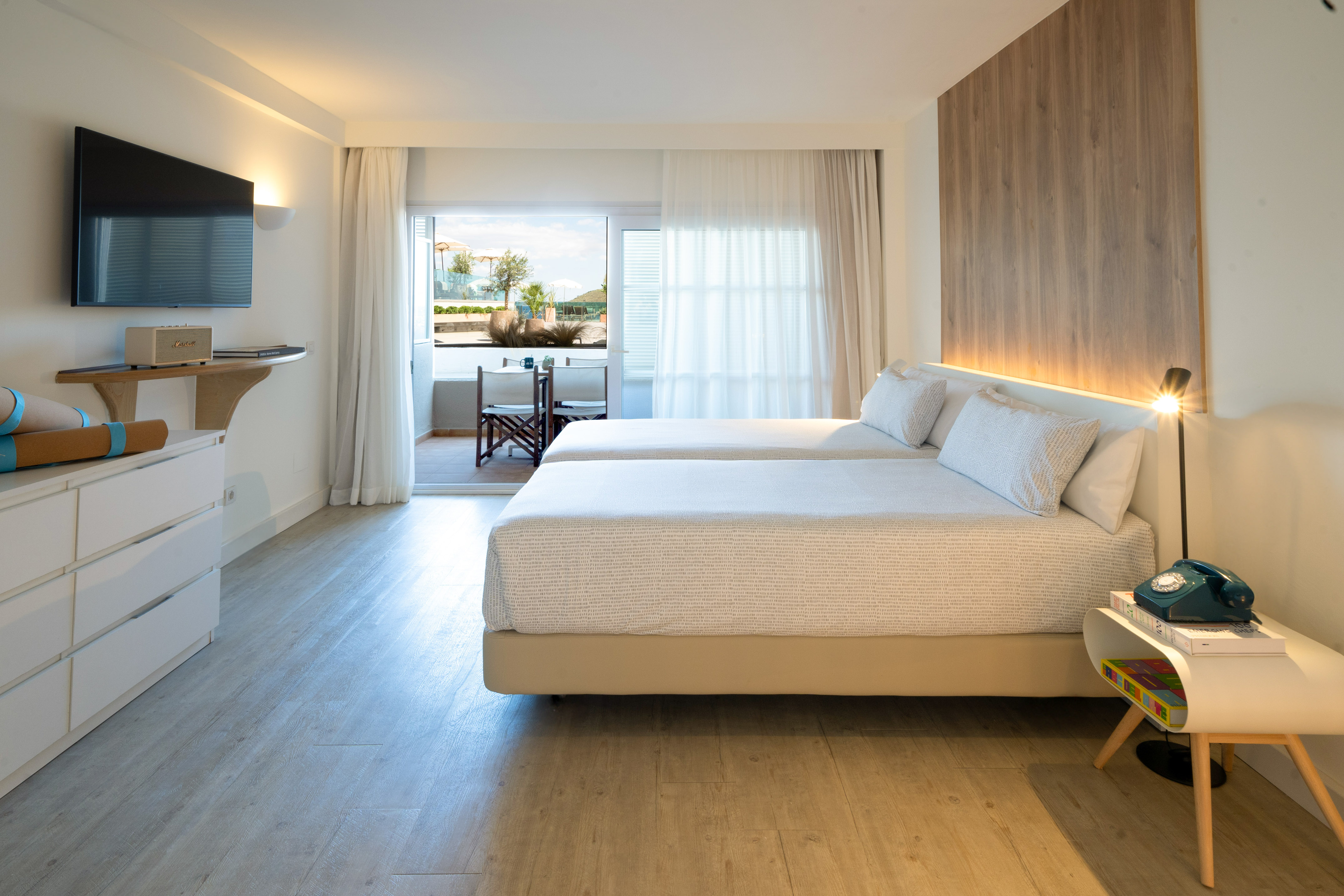 Bright modern hotel room with twin beds, balcony, TV, and wooden details.