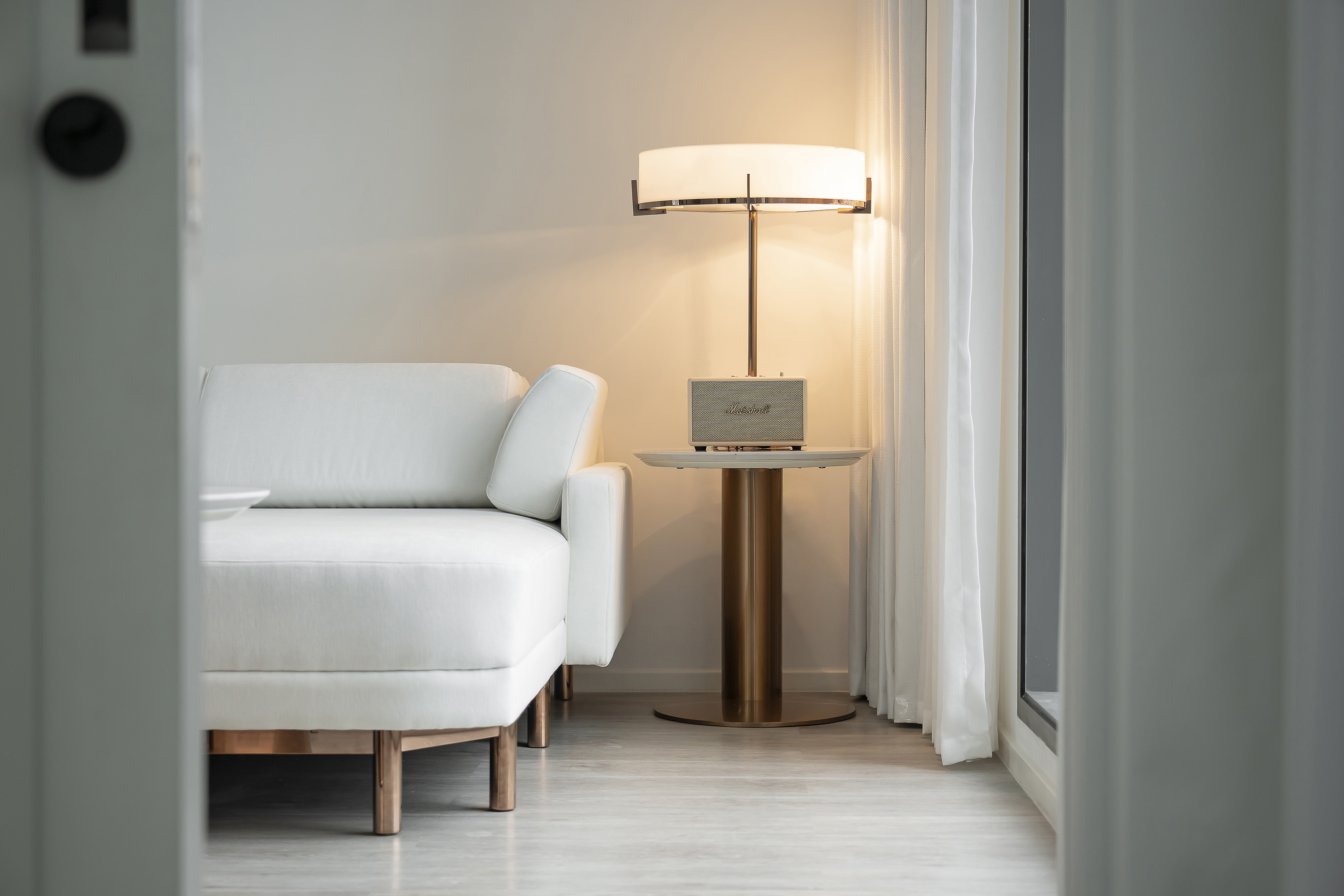 Minimalist living room with white sofa, Marshall speaker on side table, and floor lamp.