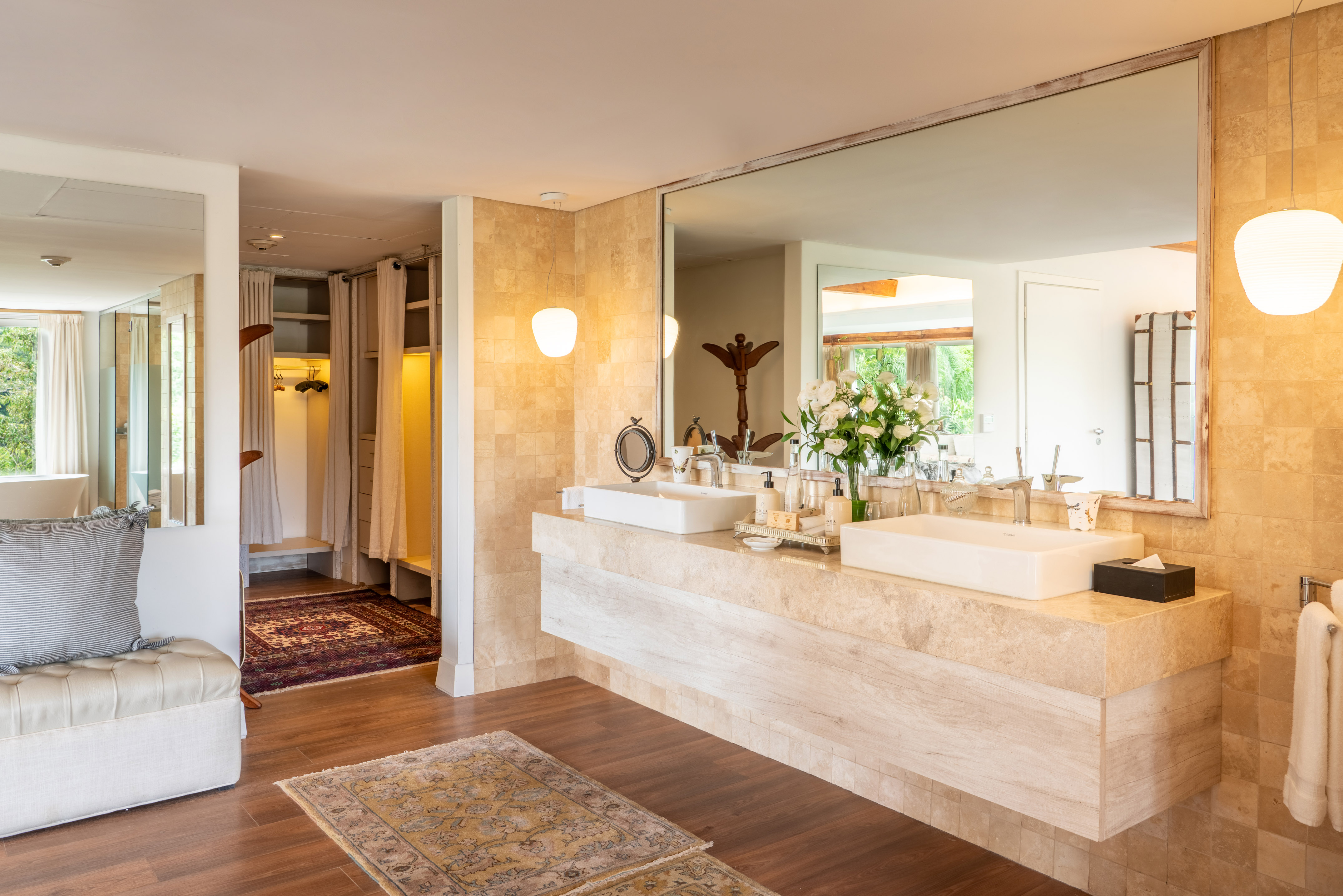 Modern bathroom with double vanity, large mirror, travertine, and dressing room.