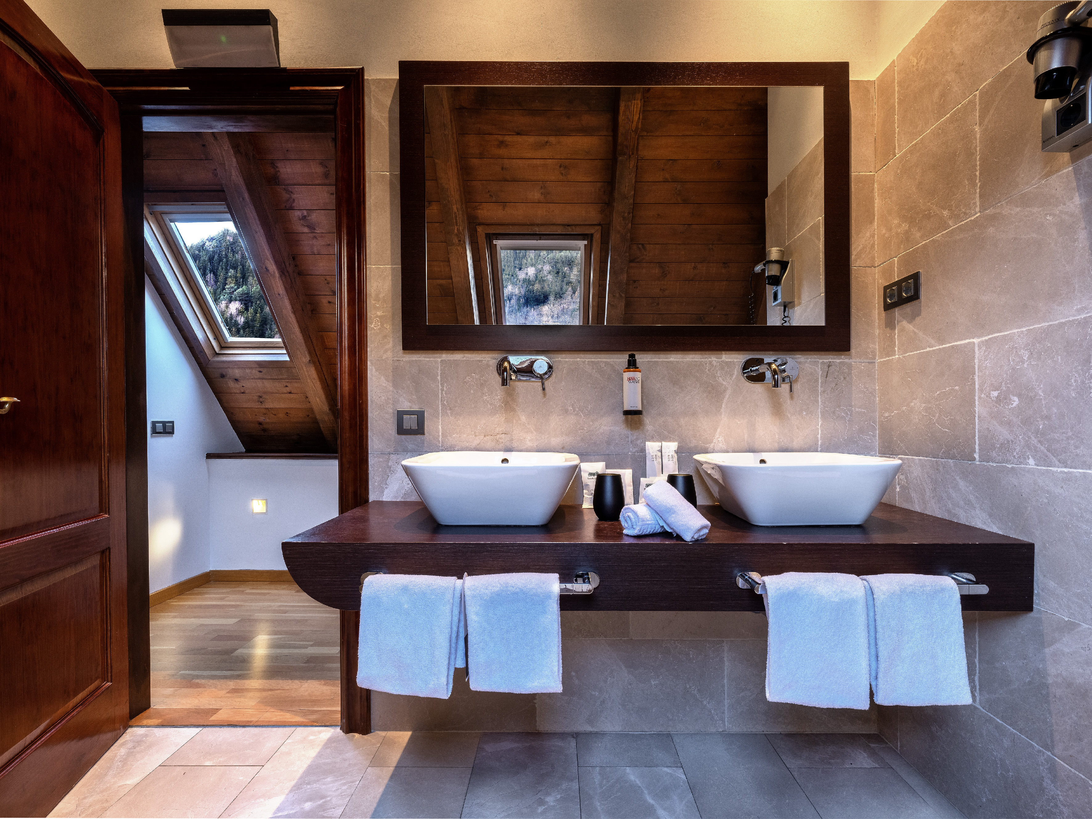 Modern hotel bathroom with double sinks, wood ceiling, and mountain view.