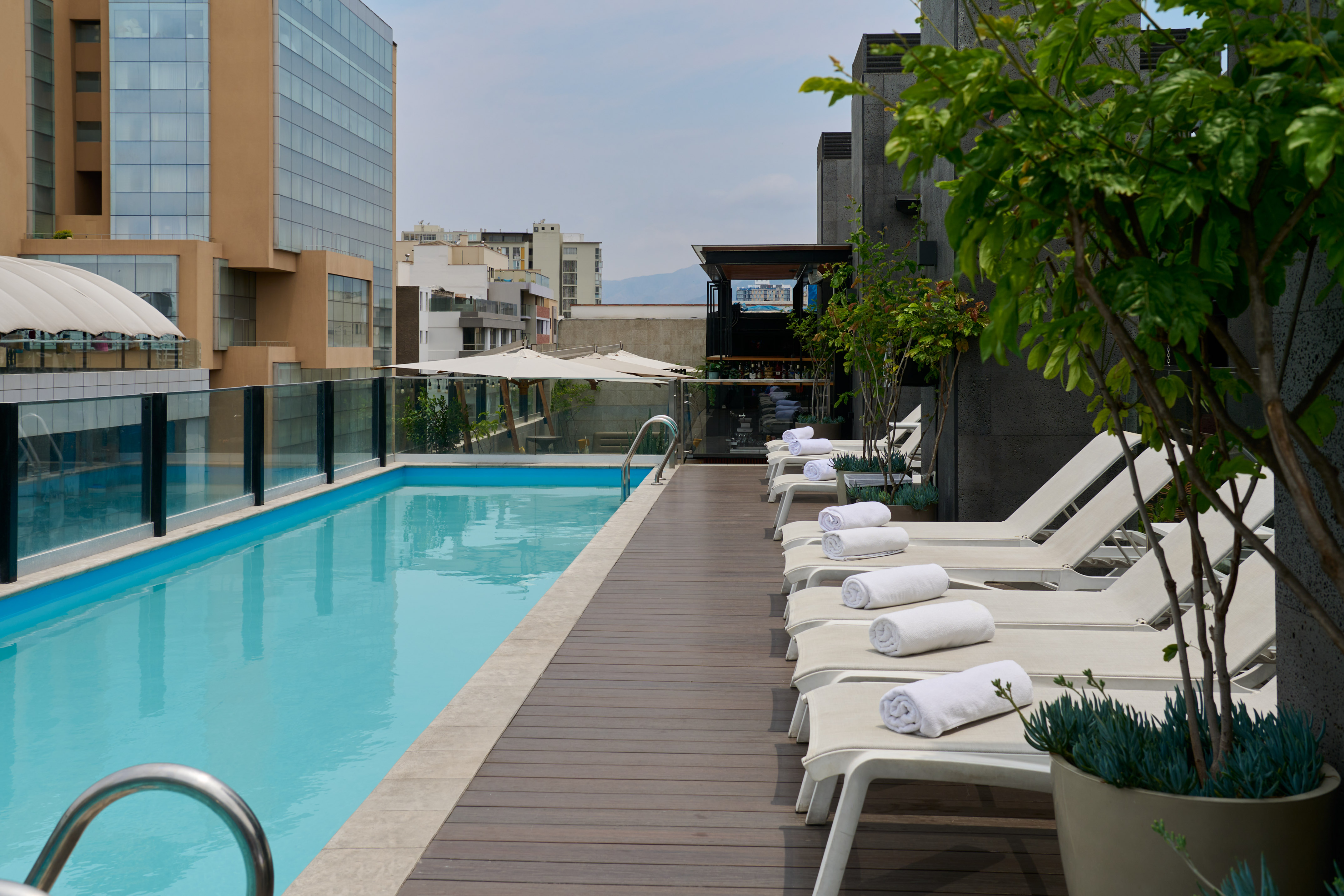 Modern rooftop hotel pool deck with lounge chairs and city views.