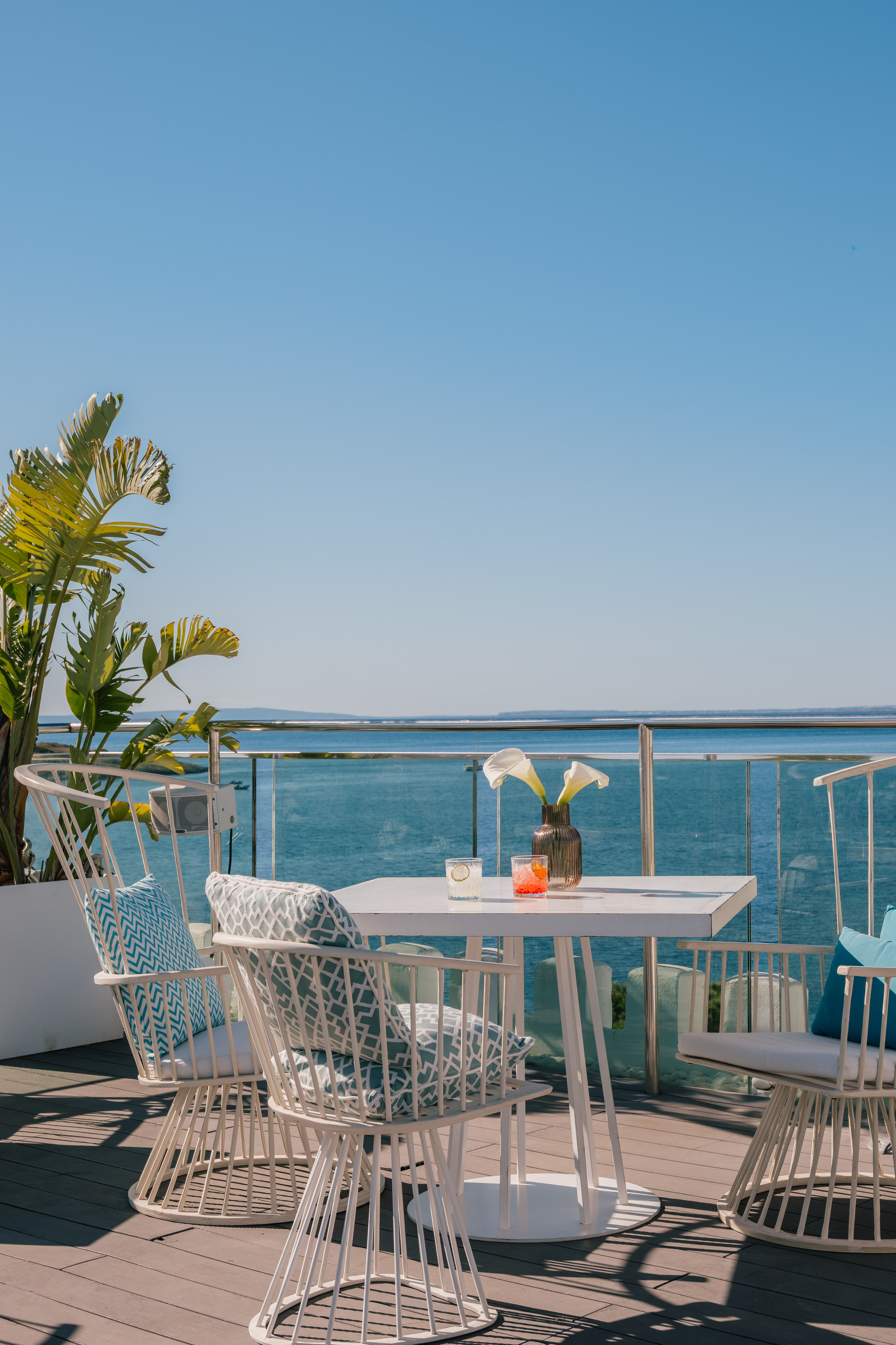 Oceanfront balcony with white patio furniture, drinks, and tropical plant.