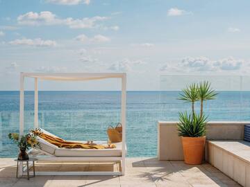 Luxury resort patio with ocean view, white daybed, and potted plant.