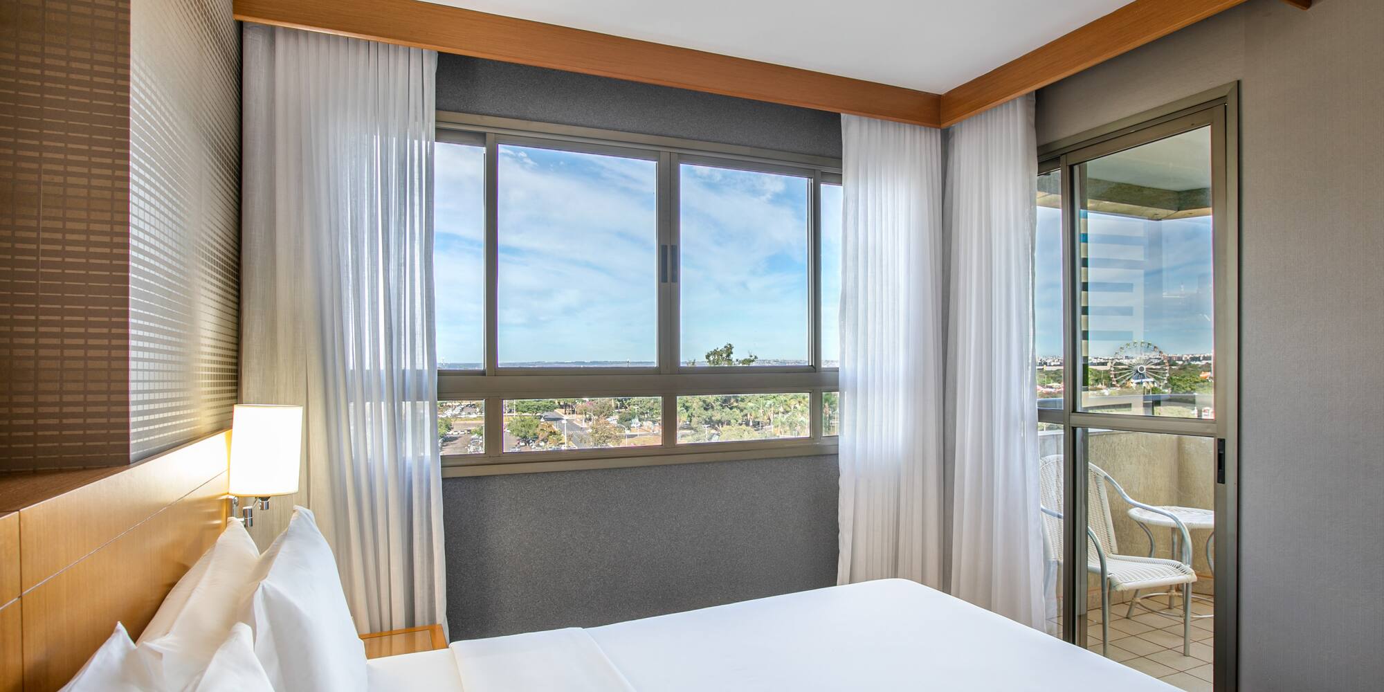 Modern hotel bedroom with large bed, city view, and balcony.