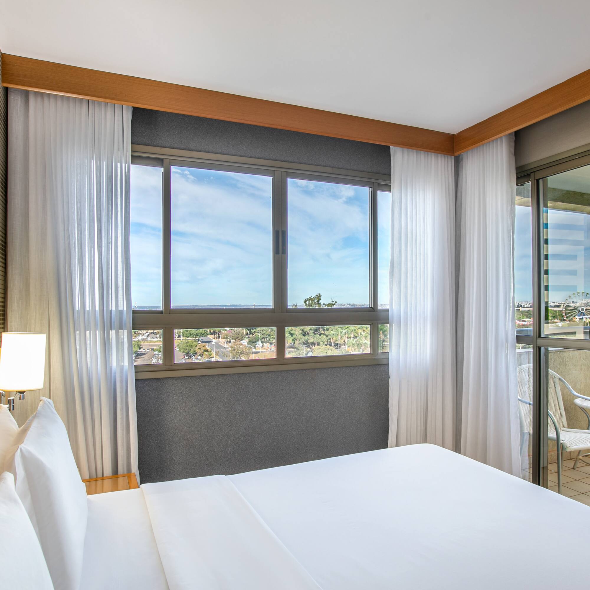 Modern hotel bedroom with large bed, city view, and balcony.