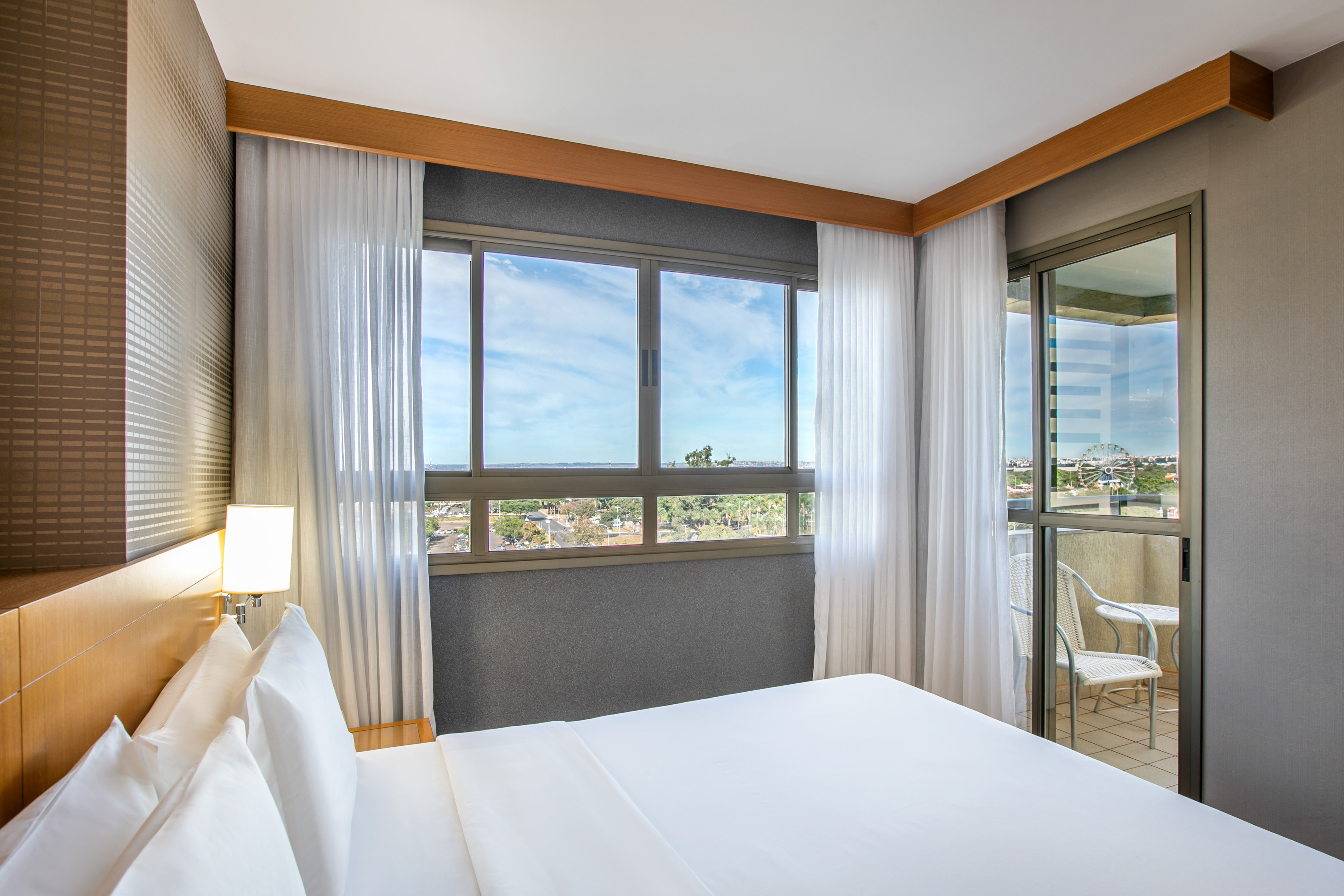 Modern hotel bedroom with large bed, city view, and balcony.