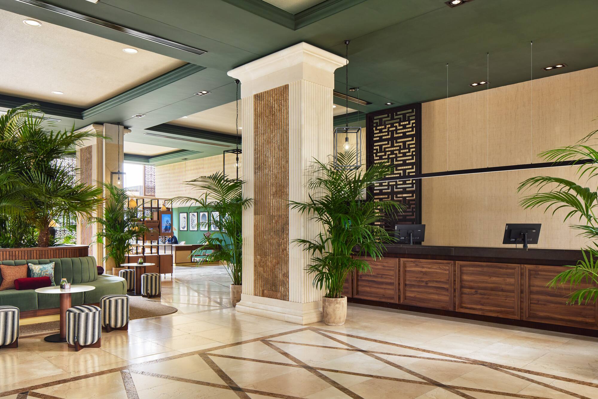 Elegant hotel lobby with green sofa, palm plants, and modern reception desk.
